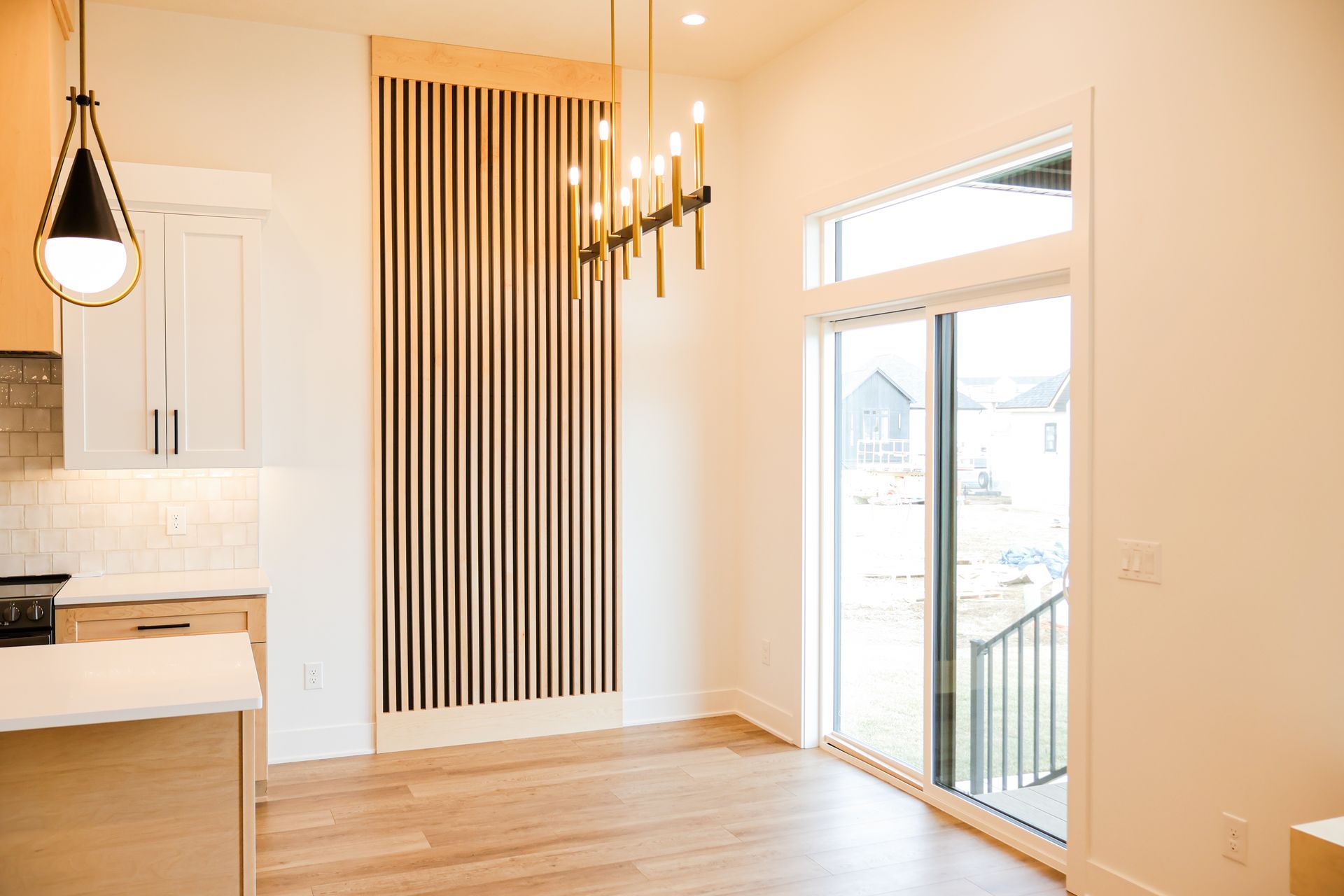 Dining area with vertical wood paneling, chandelier, and sliding glass door. Kitchen visible on left.