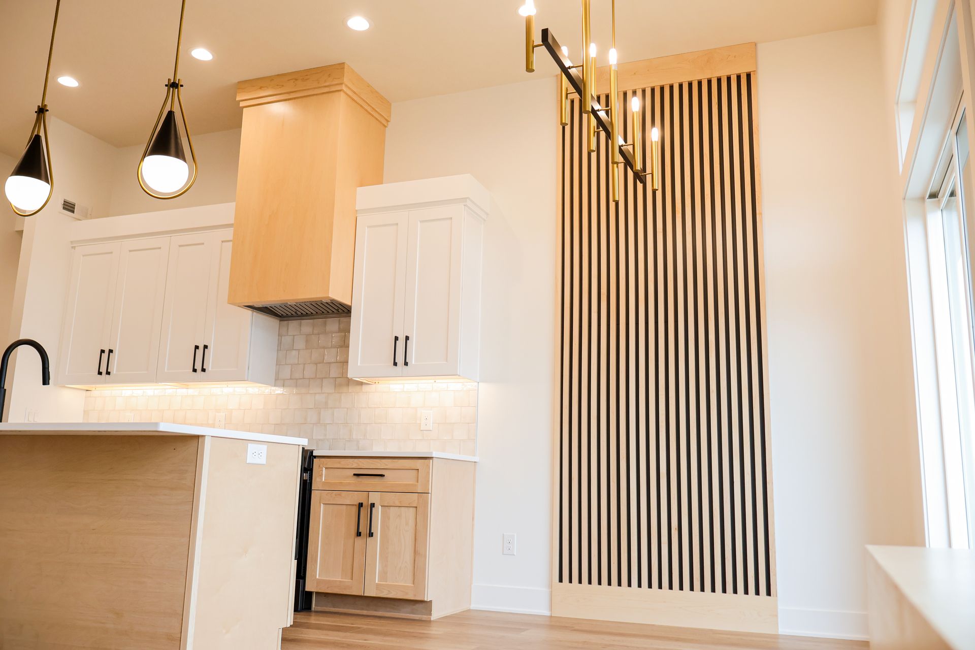 A two-story living room with white paneled walls, a tiled fireplace with a white mantel, an arched pane-style mirror, a tall black floor lamp and light wood flooring.