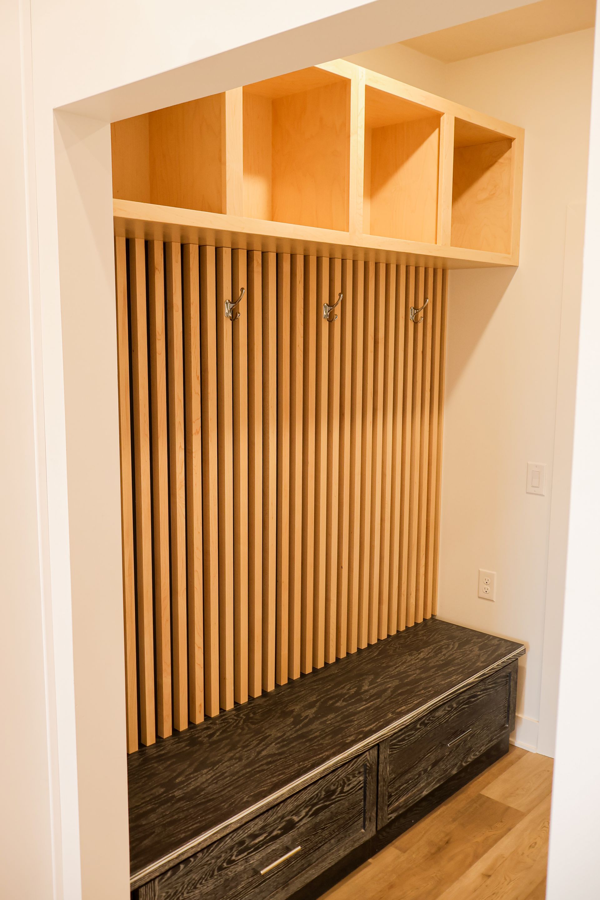 Built-in entryway storage with wood paneling, bench, and cubbies. Natural wood tones.