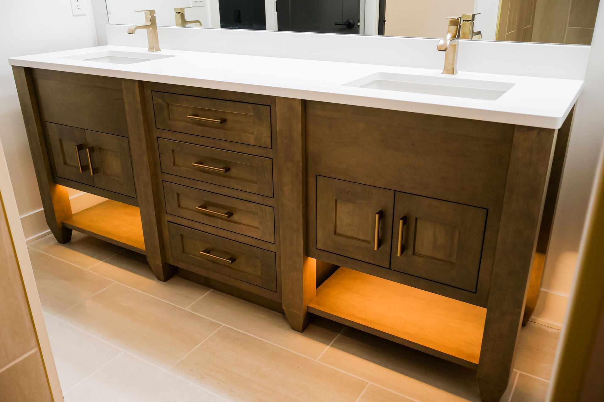 Wooden bathroom vanity with two sinks, gold fixtures, and under-cabinet lighting.