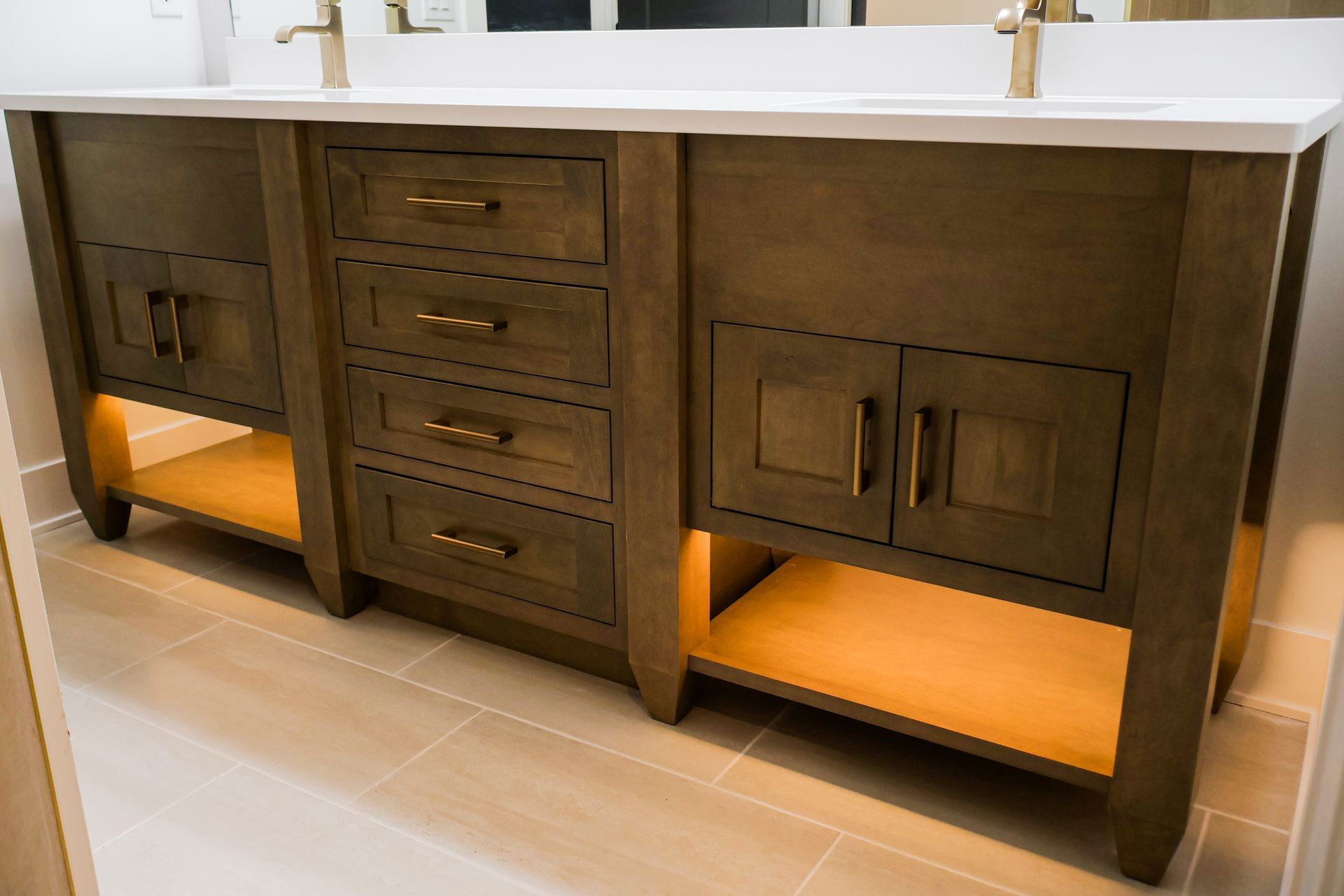 Wooden bathroom vanity with drawers, cabinets, and open shelving illuminated by warm lighting.