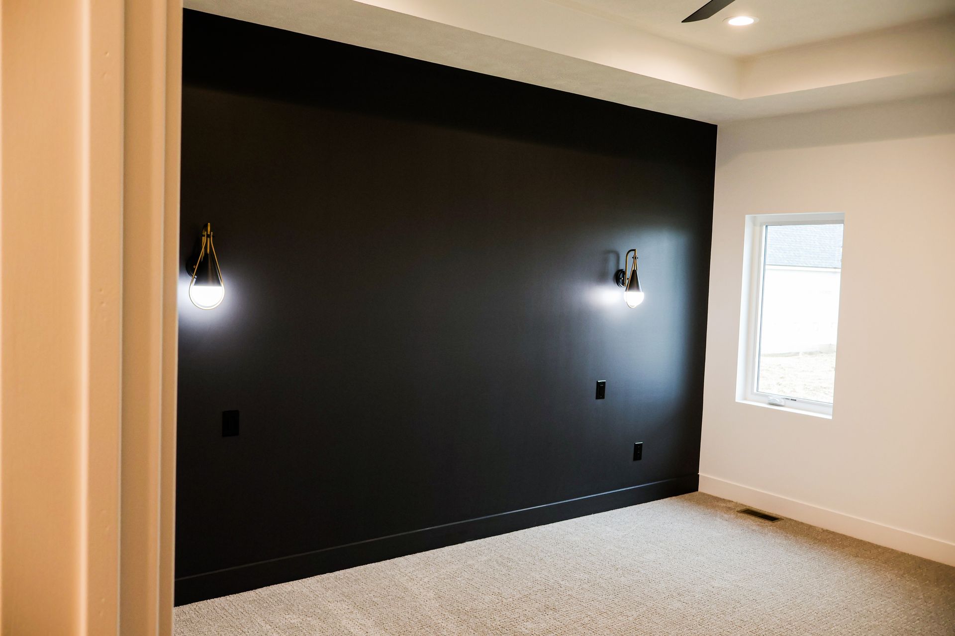 Bedroom with black accent wall, sconce lighting, white trim, window, and beige carpet.