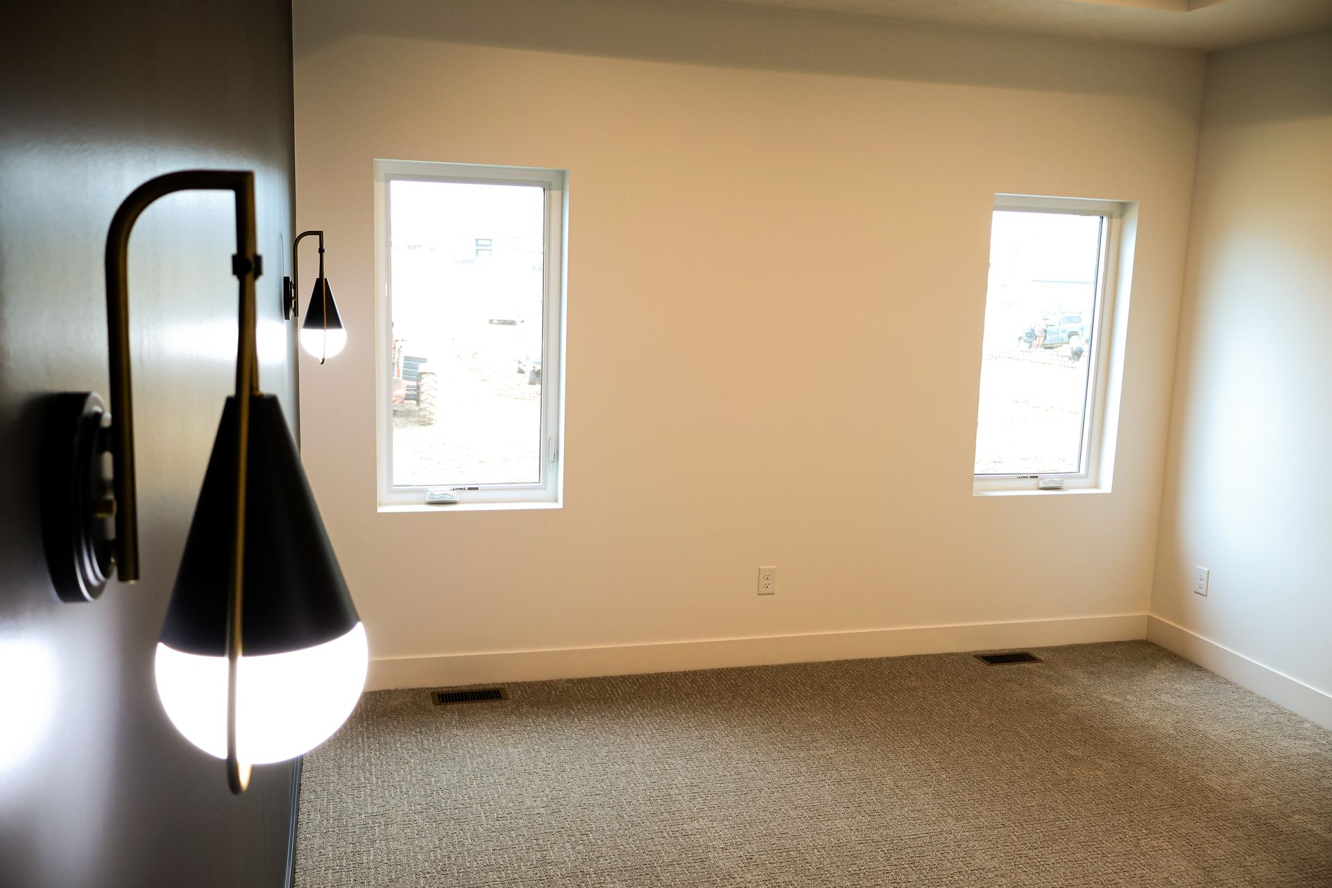 Bedroom interior with wall sconce, two windows, and neutral carpet.