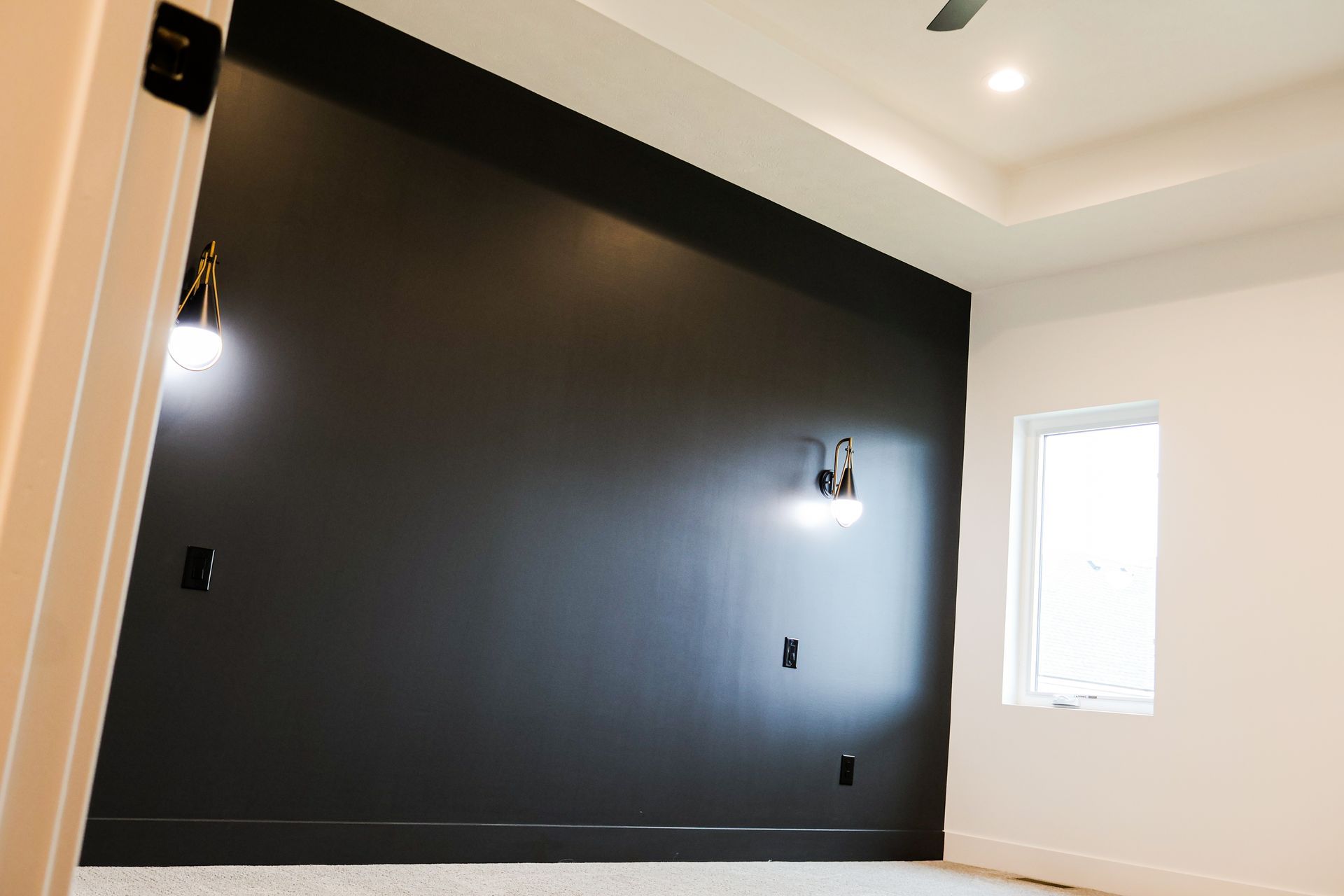 Black accent wall in a bedroom with sconces, outlets, a small window, and a white ceiling.