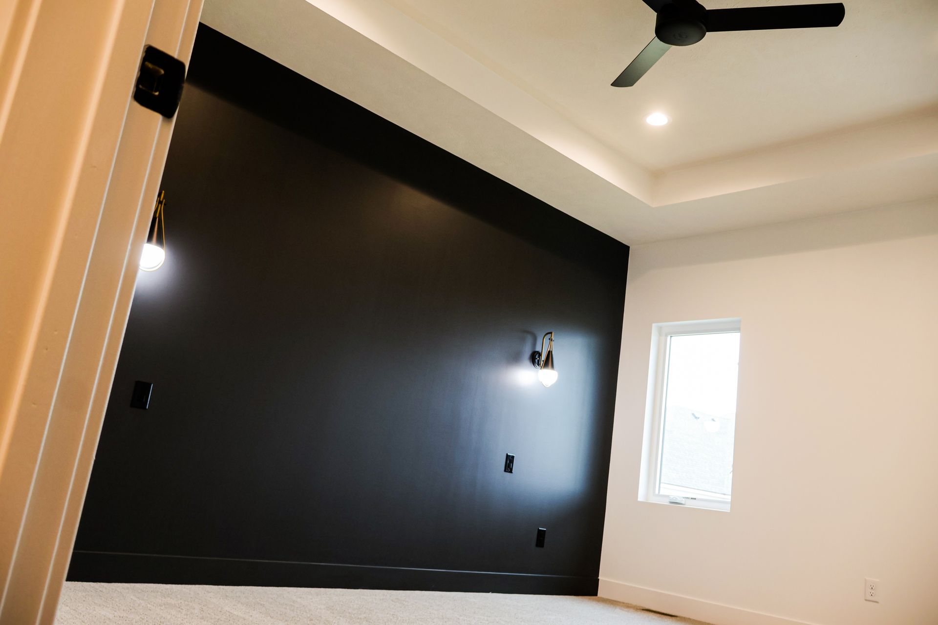 Black accent wall in a modern bedroom with a ceiling fan and window.