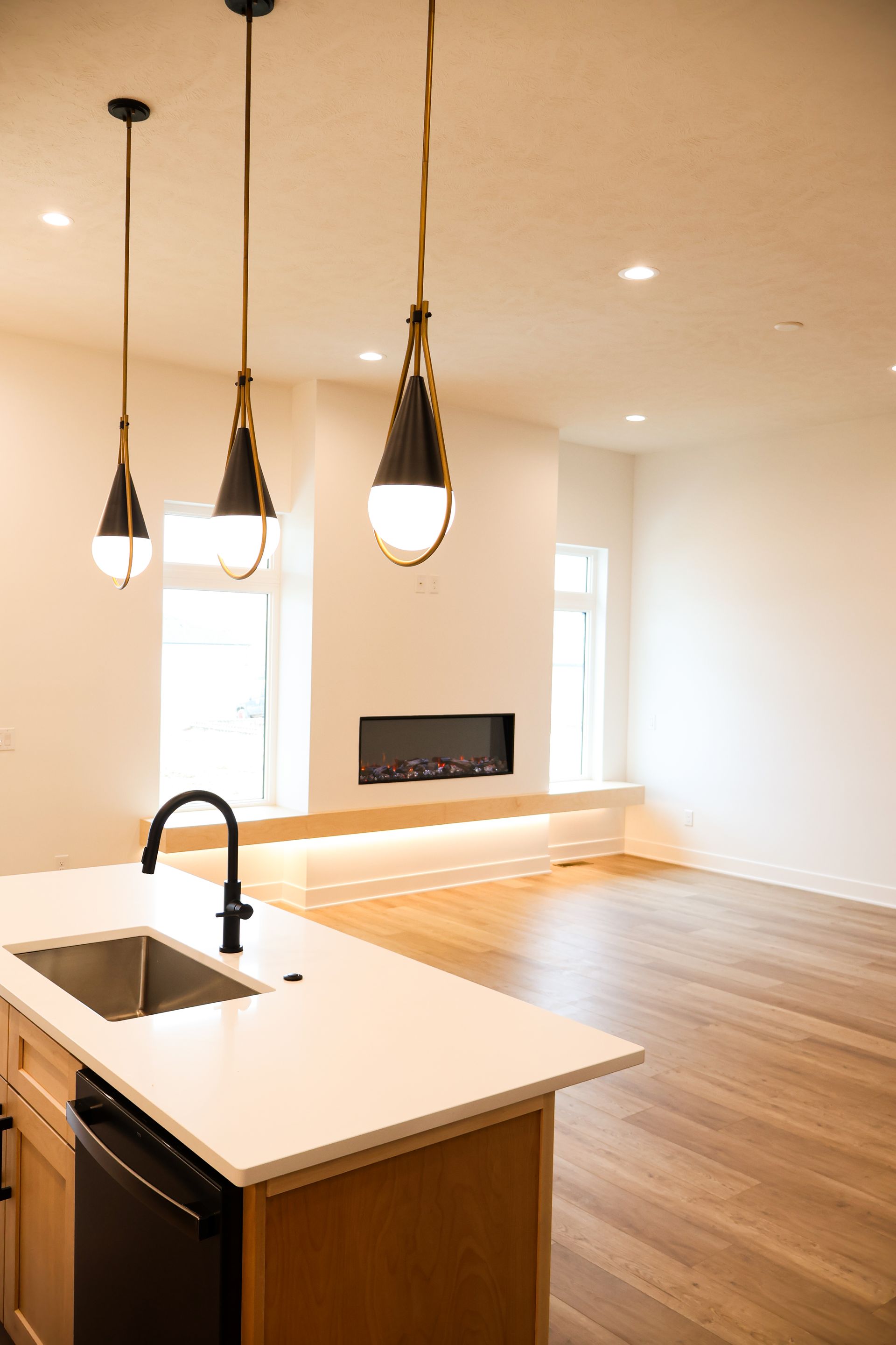 Kitchen with island and sink, pendant lights hanging, fireplace, hardwood floors, and white walls.