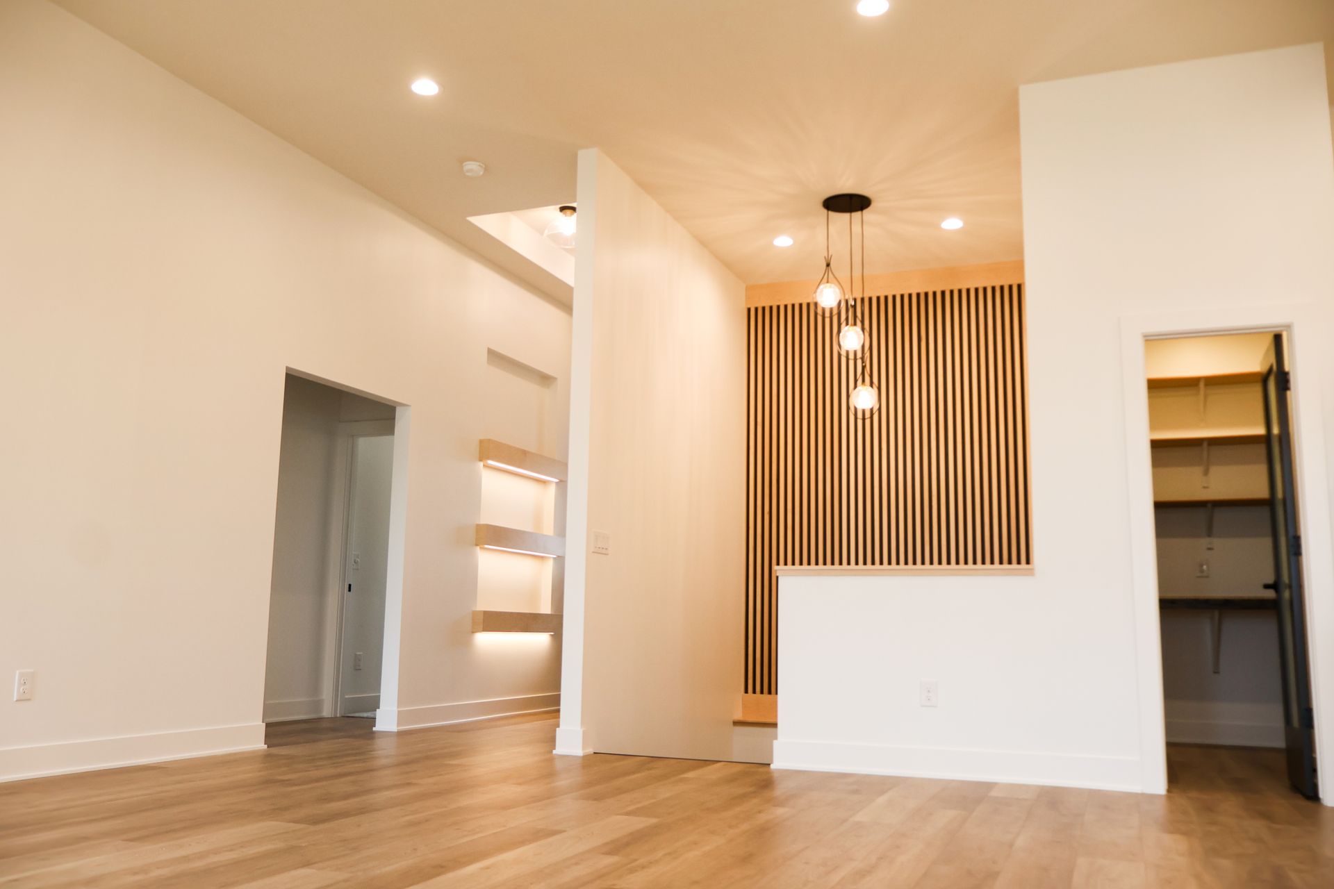 A living area with a linear fireplace in a white wall, a lit floating wood hearth shelf, a gold chandelier, a sliding patio door and wood-look floors.
