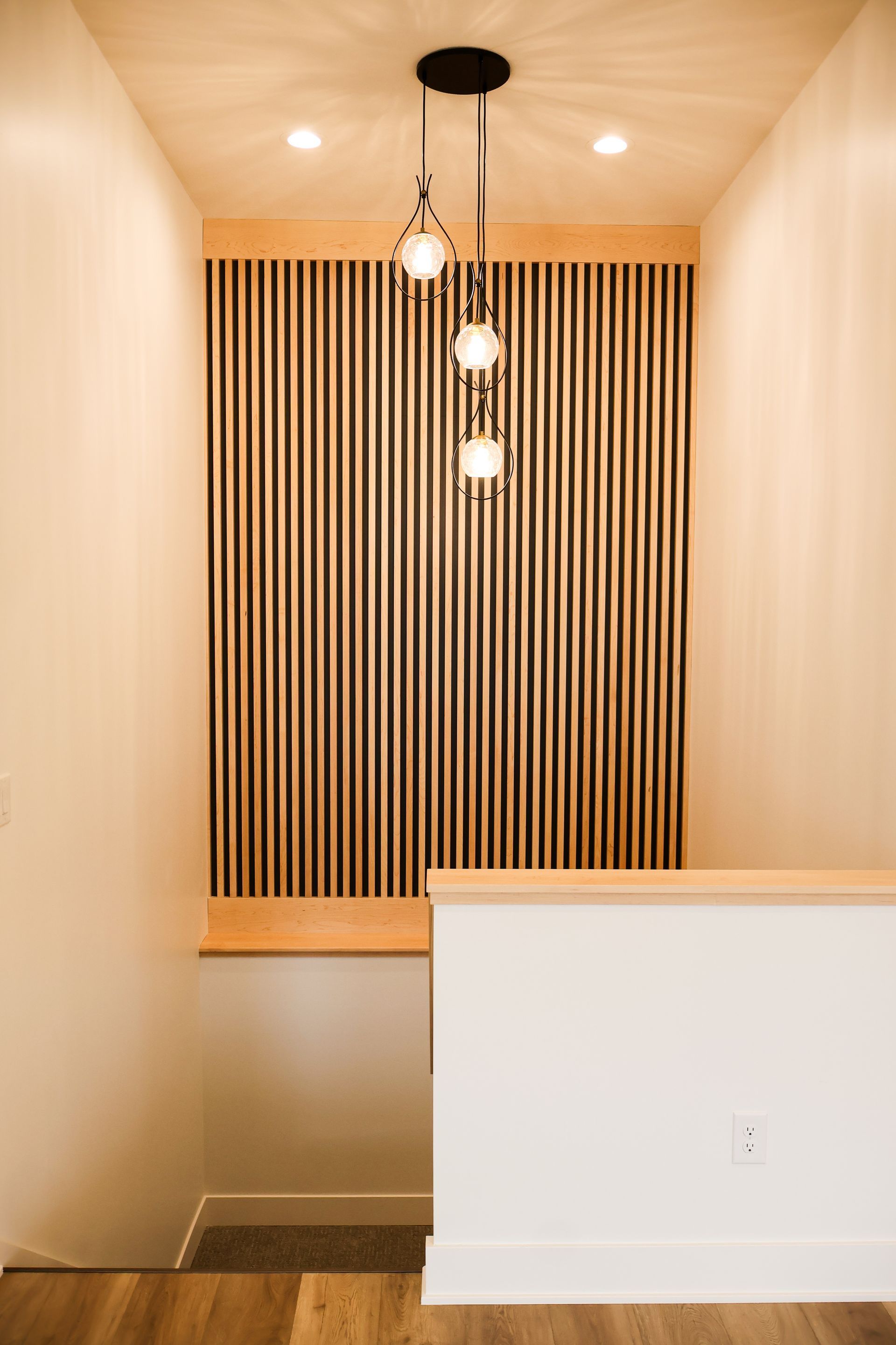 Hallway with wood slat accent wall, pendant lights, and staircase.