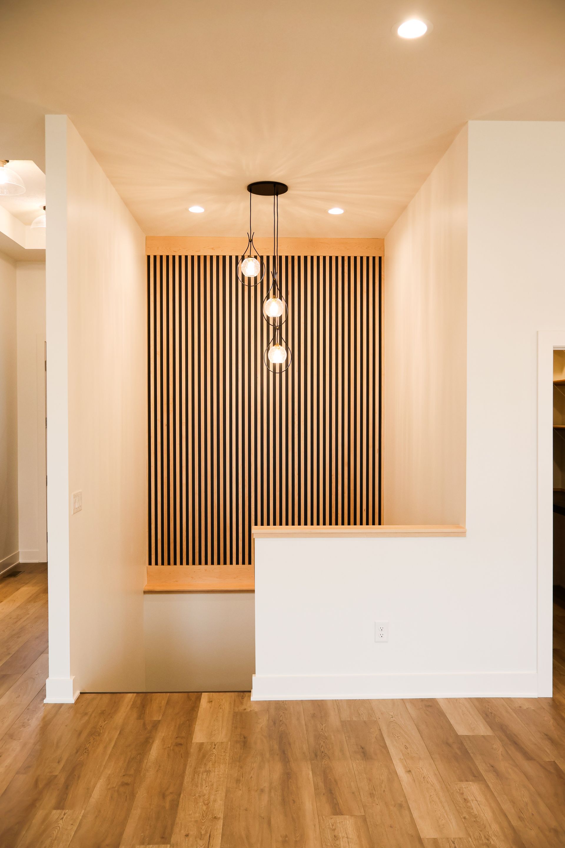 Hallway with wooden floor, slatted wood accent wall, built-in bench, and pendant light fixture.