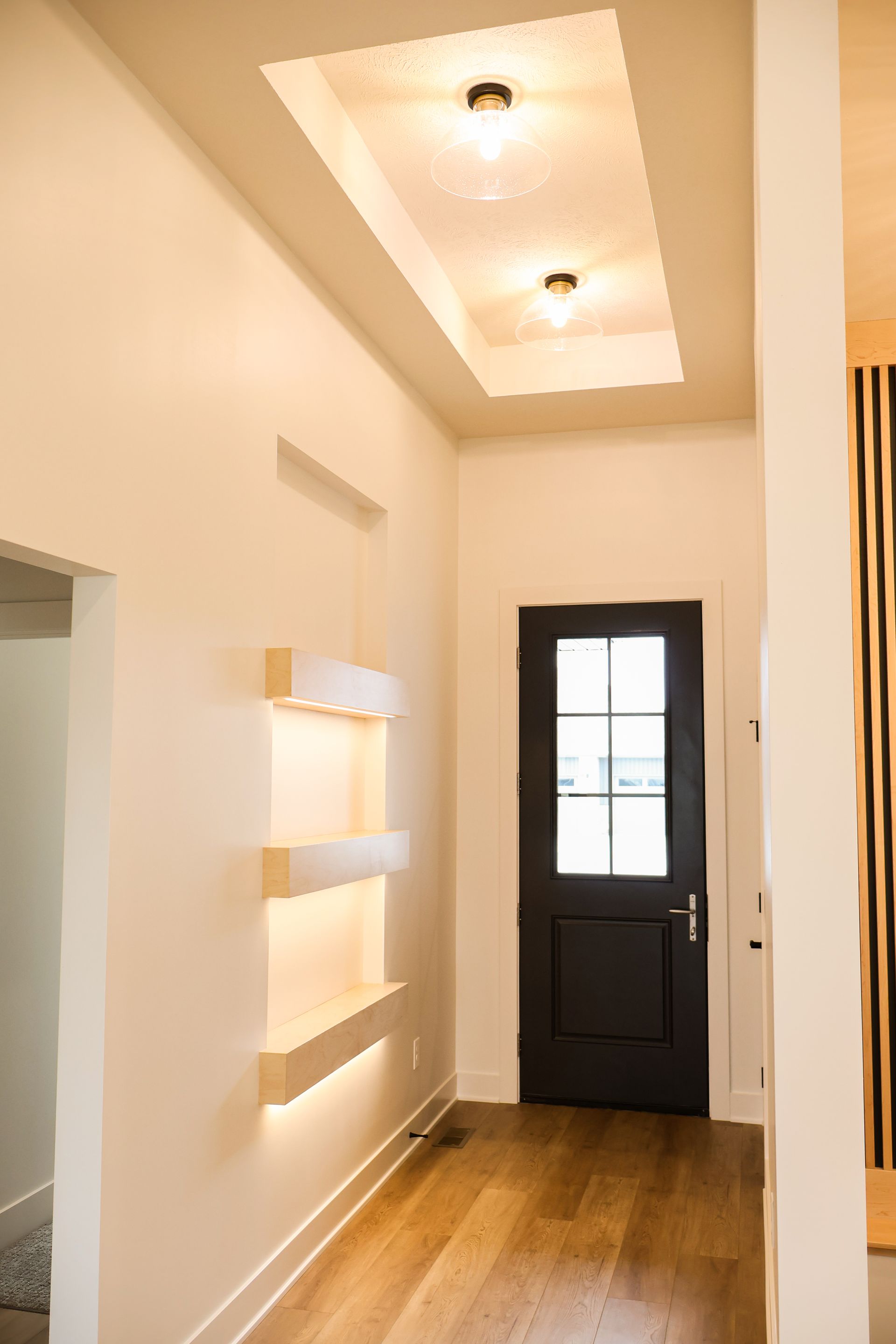 Entryway with black door, recessed ceiling with lights, built-in shelves.