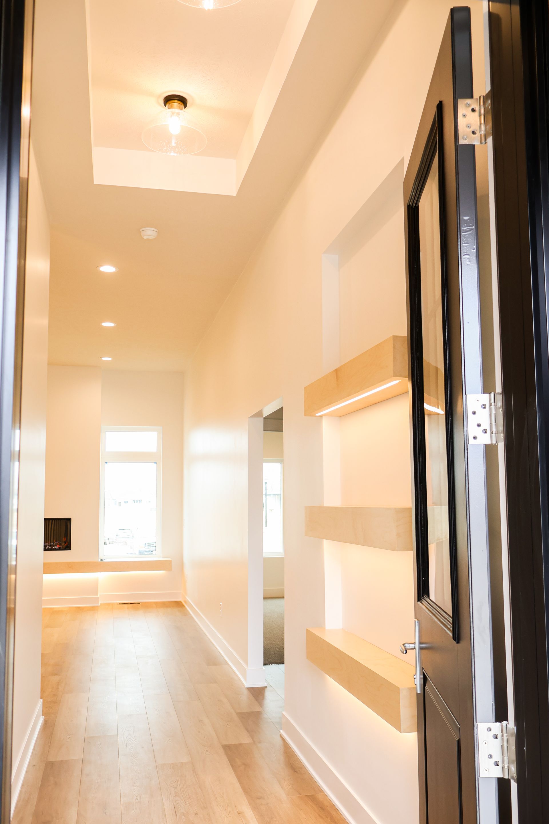 An empty bedroom with gray walls, gray carpet, a white paneled door, a ceiling fan and a large double window.