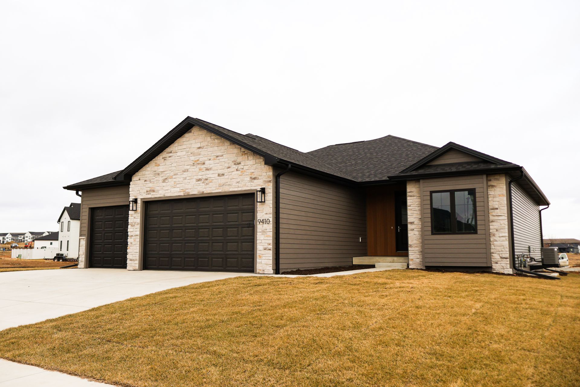 Modern single-story house with gray and brick facade, dark garage door, and brown front door.
