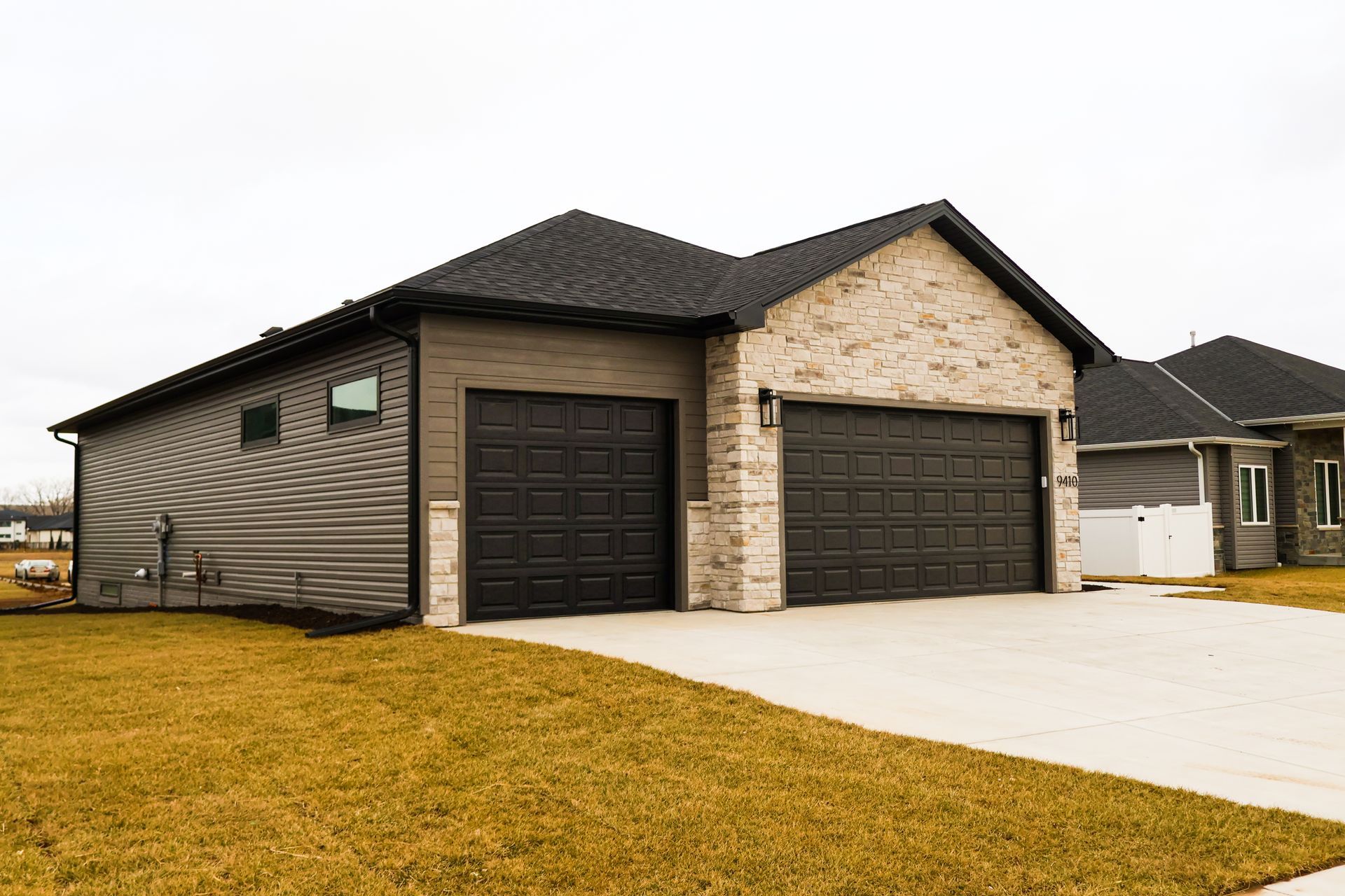 Two-car garage with dark brown doors, light brick facade, and gray siding, on a cloudy day.