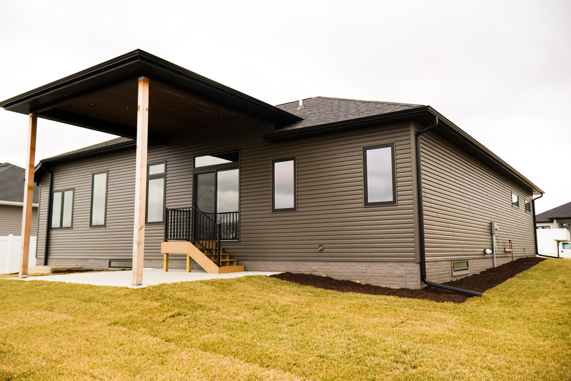 Modern house exterior with covered patio, brown siding, and dark roof.