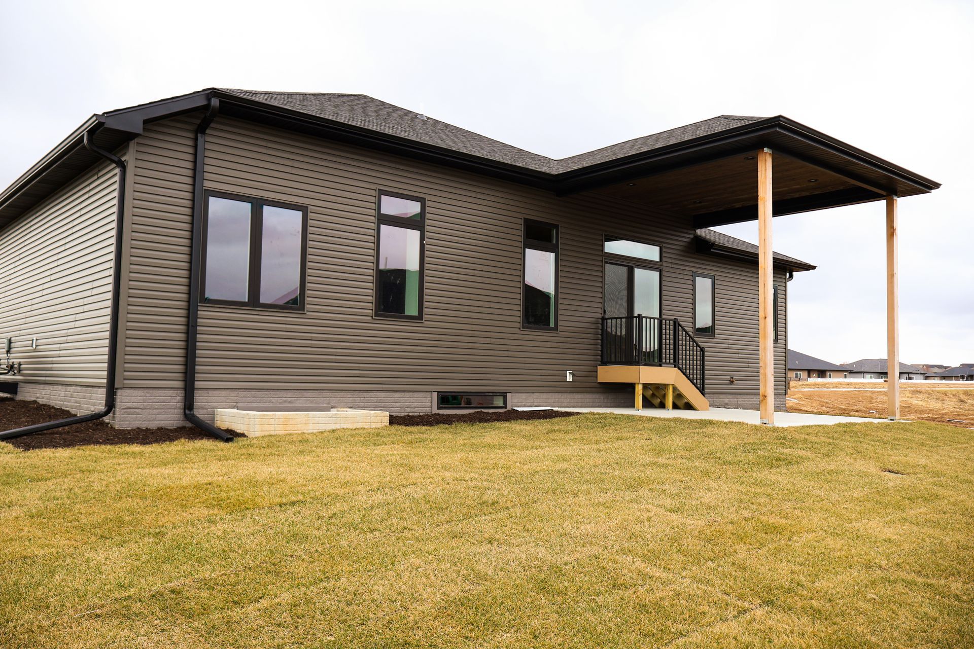 A gray house with a covered patio, black windows, and a grassy yard.