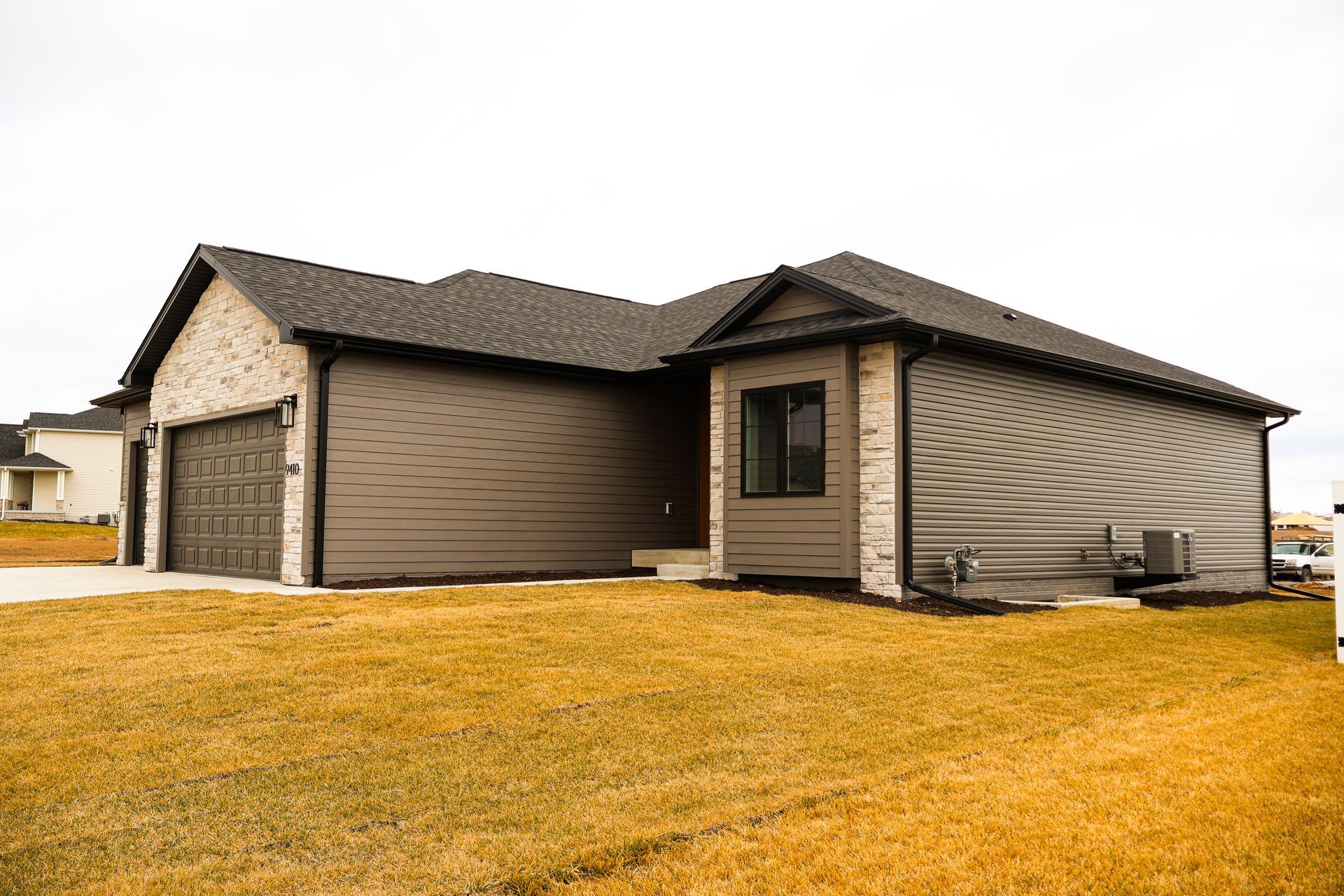 Tan and gray house with a dark roof and brick accents on a lawn.