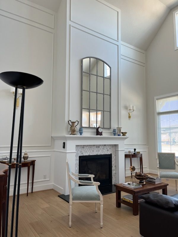 A bedroom with a tray ceiling, a black accent wall with two sconces, beige carpet, a black ceiling fan and doorways to a closet and bathroom.