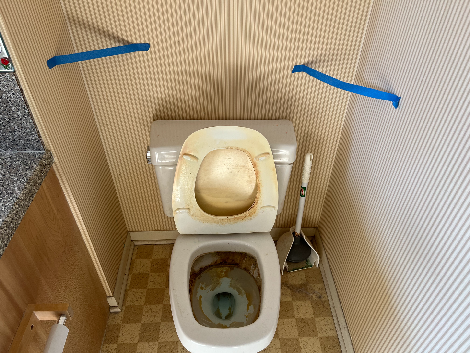 A toilet in a bathroom with tape on the wall.