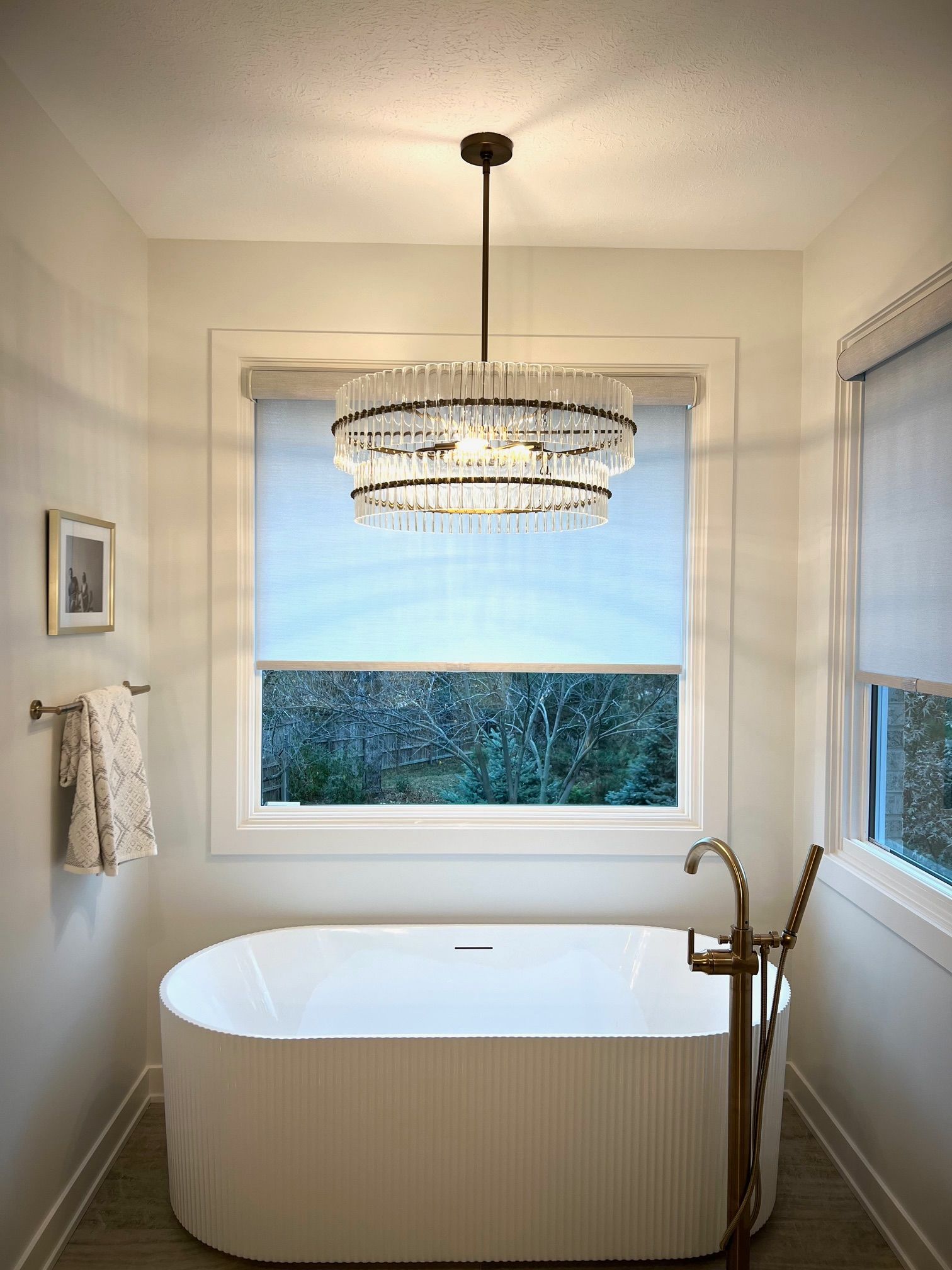 Bathroom with a modern oval tub, window, and tiered crystal chandelier.