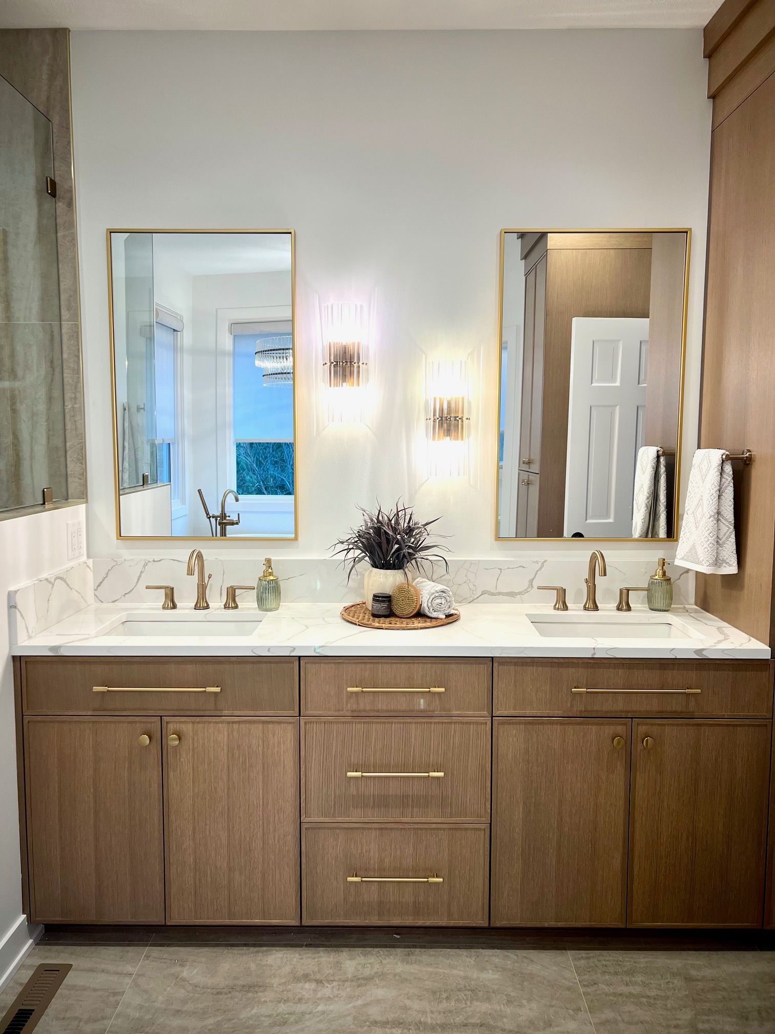 Bathroom with double vanity, light wood cabinets, gold fixtures, marble countertop, and rectangular mirrors.