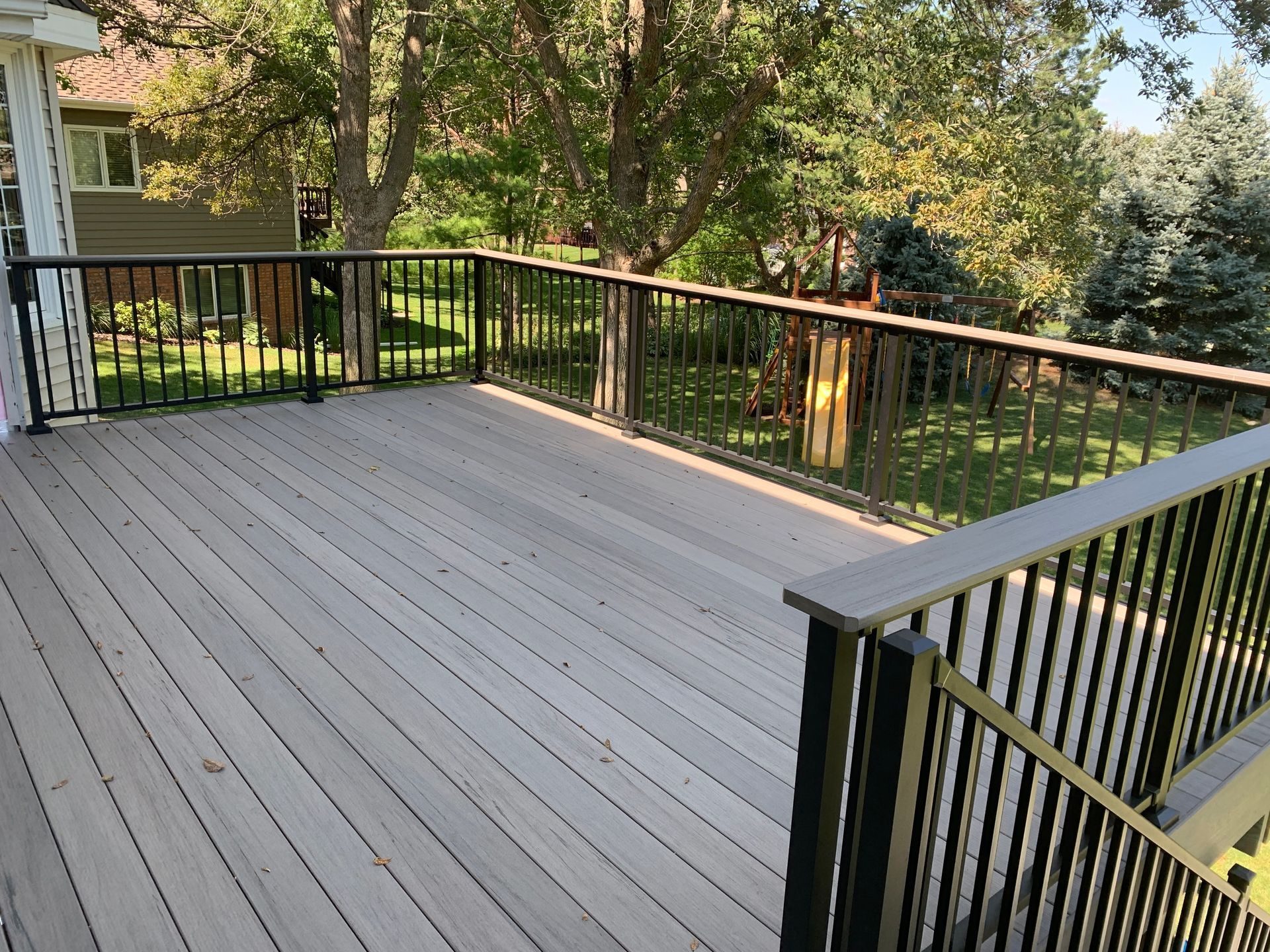 A wooden deck with a metal railing and trees in the background