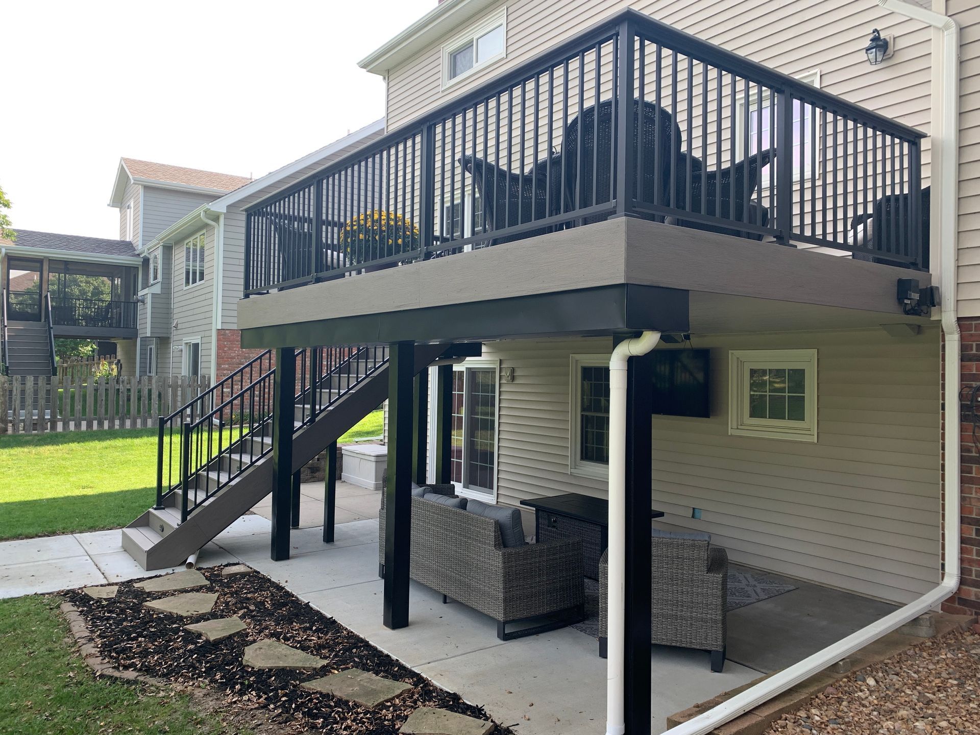 A large deck with stairs leading up to it is in the backyard of a house.