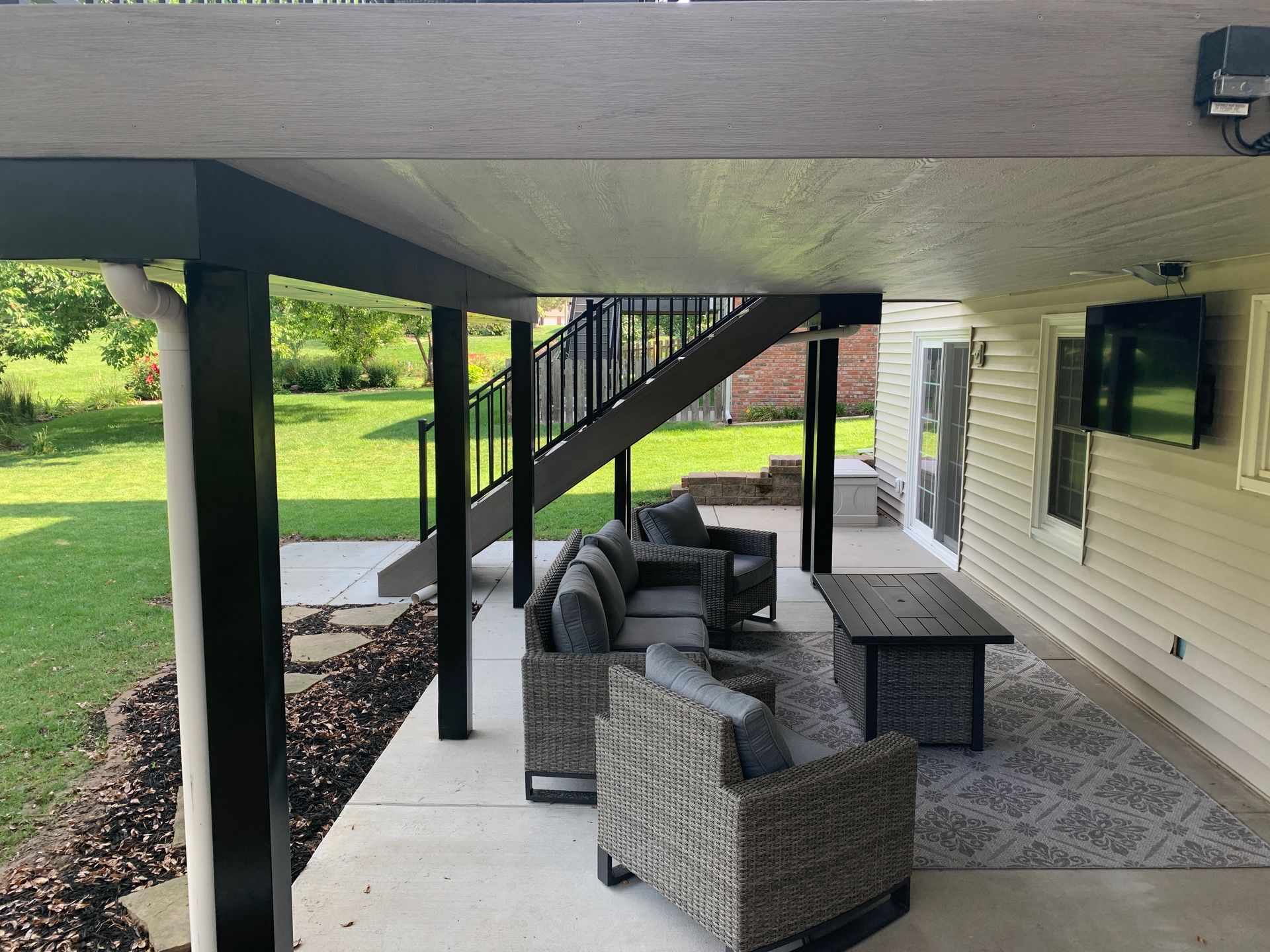 A covered patio with a couch , chairs , table and television.