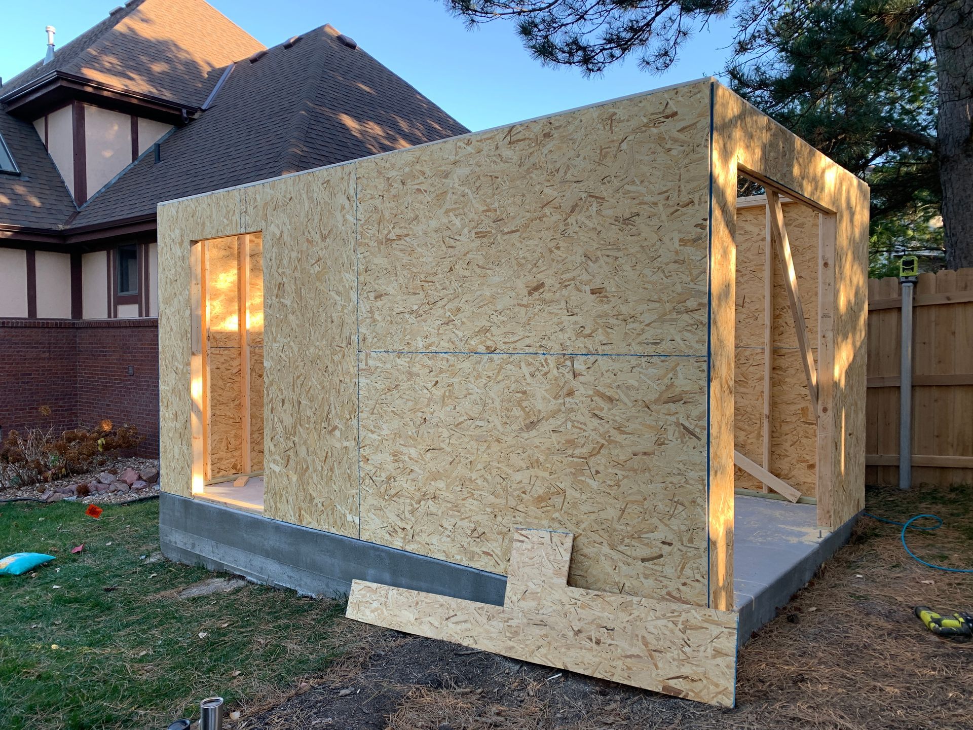 A wooden shed under construction in a grassy backyard, with a house in the background.
