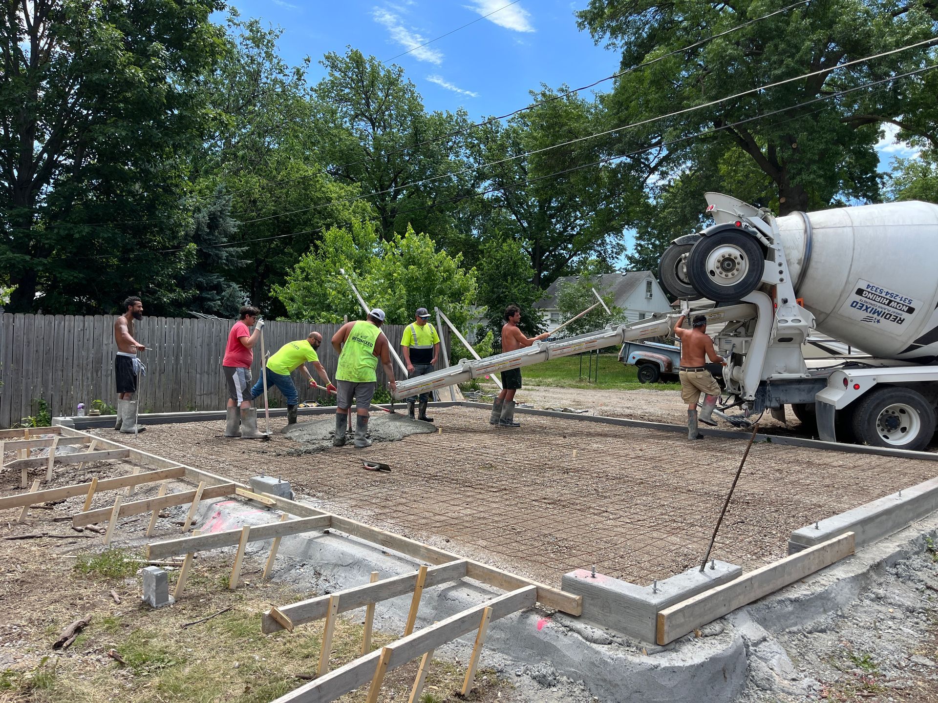Construction workers pouring concrete from a truck into a prepared foundation on a sunny day. 