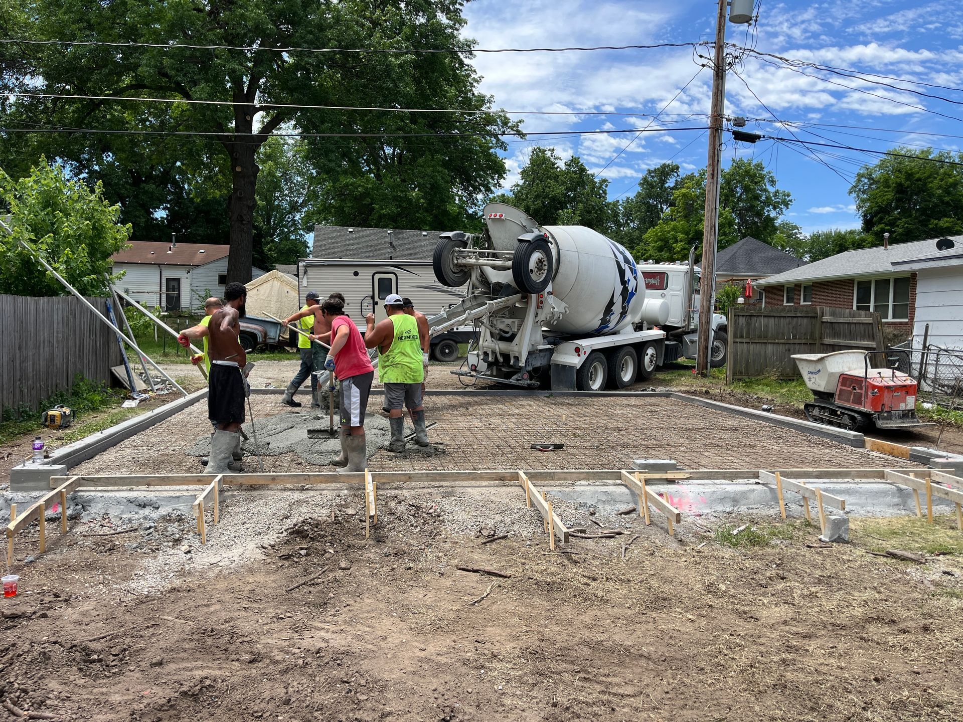 Construction workers pouring concrete from a truck into forms at a residential construction site on a sunny day.