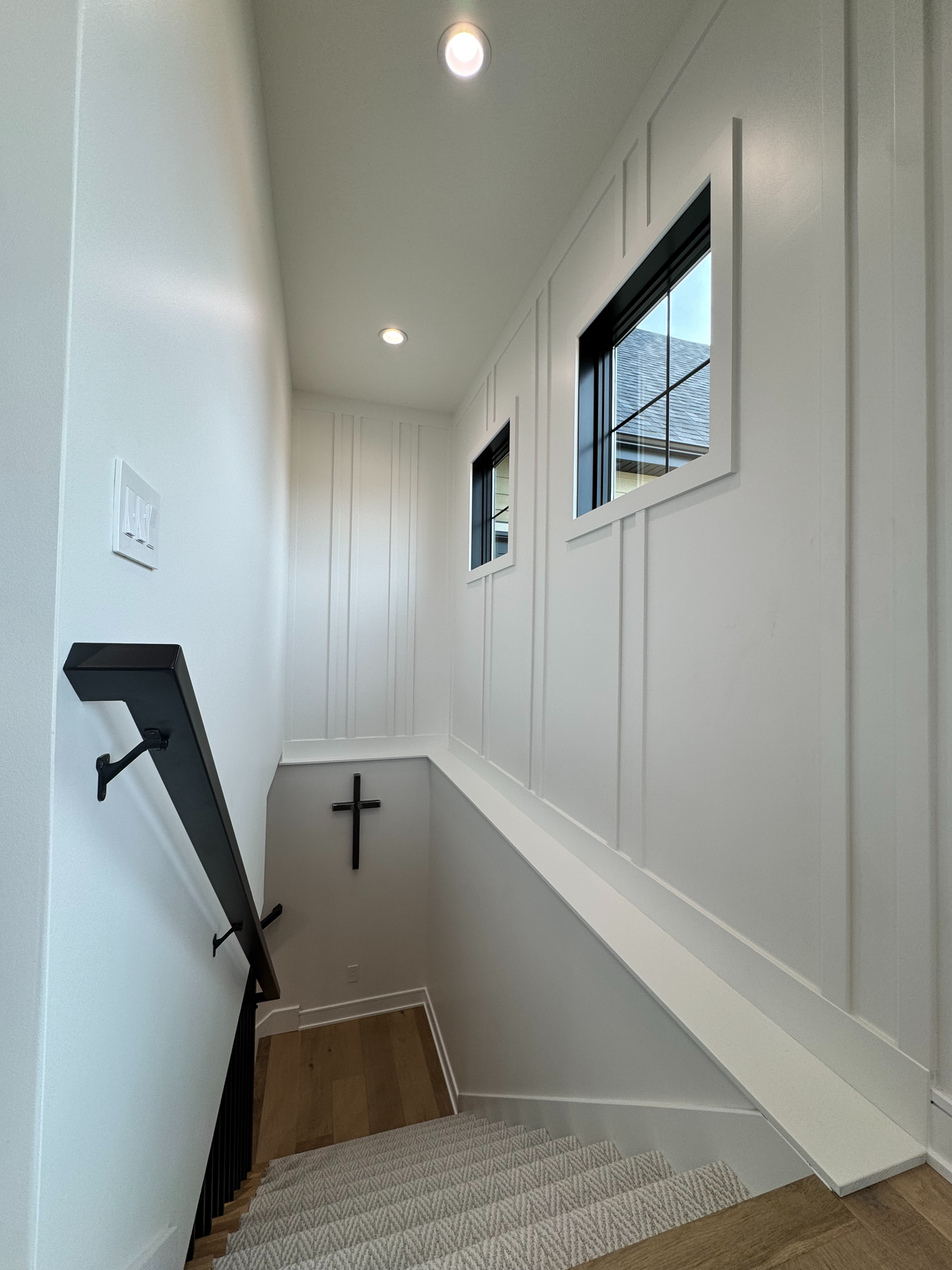 A carpeted staircase seen from below, with a vertical wood slat accent wall, a three-globe pendant light and recessed lights.