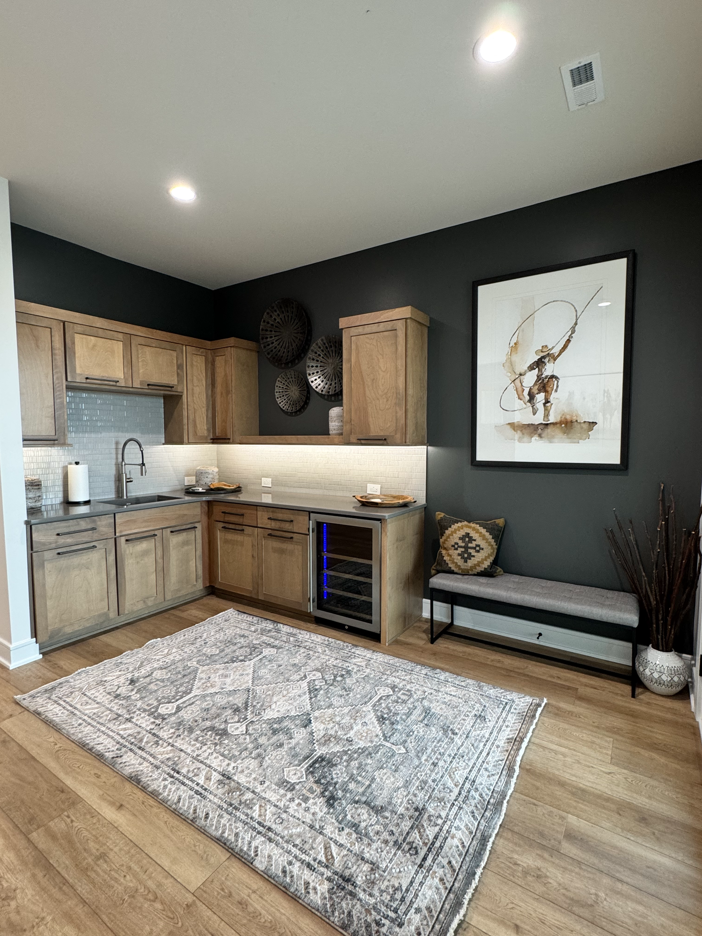 A kitchen with wooden cabinets , a rug , a refrigerator and a painting on the wall.