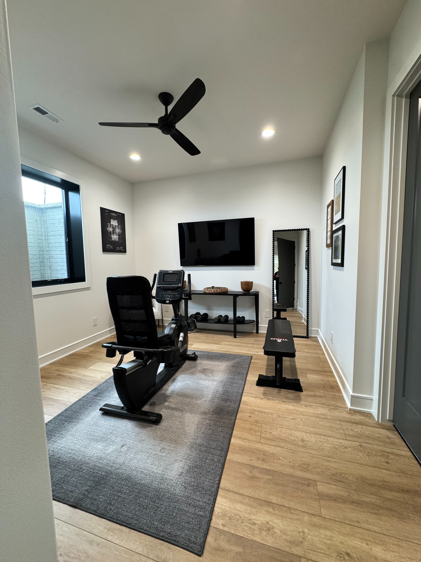 A home gym with a ceiling fan and a flat screen tv.