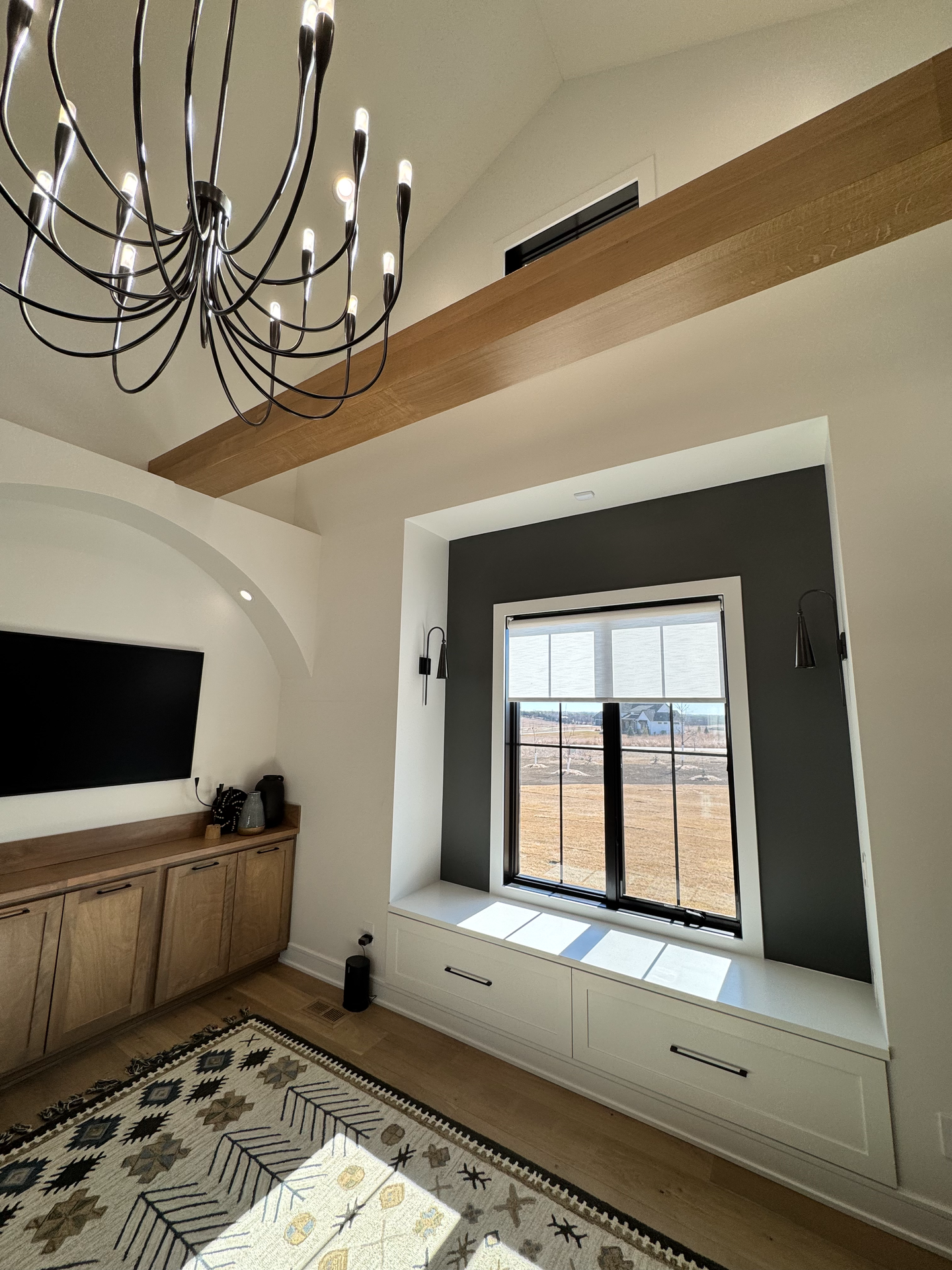 A living room with a large window and a chandelier hanging from the ceiling.