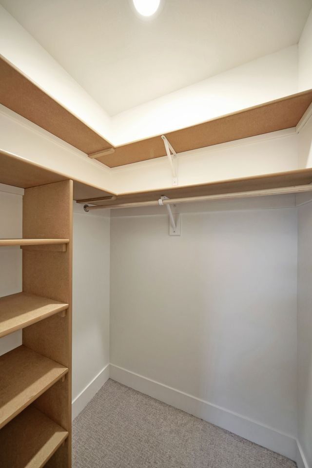 A walk in closet with wooden shelves and clothes racks.