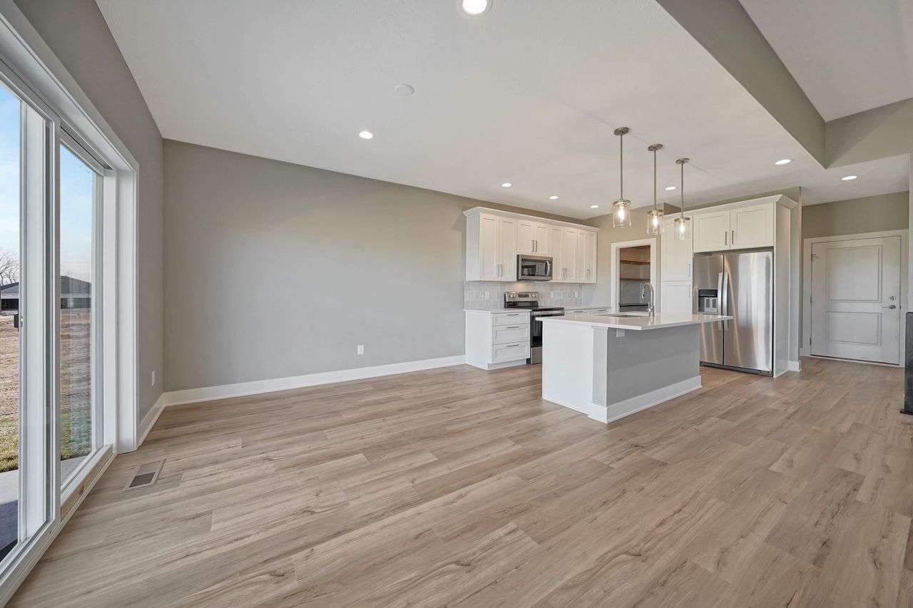 An open-plan interior with a white kitchen, a quartz island with three glass pendants, stainless appliances, gray walls and light vinyl plank floor.