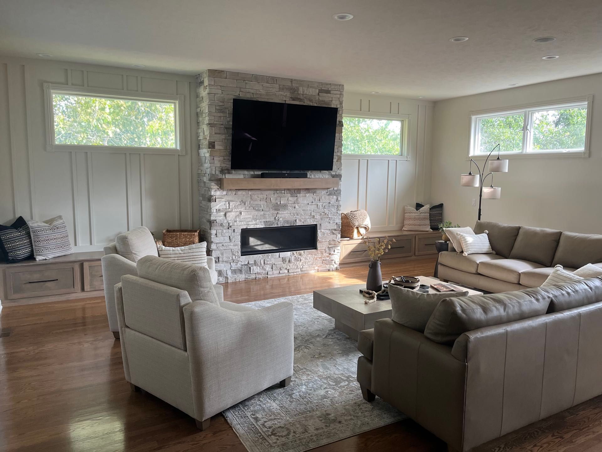 A great room with a sectional sofa, a gas fireplace framed in stacked stone, and a wall-mounted TV in a whole-home remodel, Lincoln, NE.
