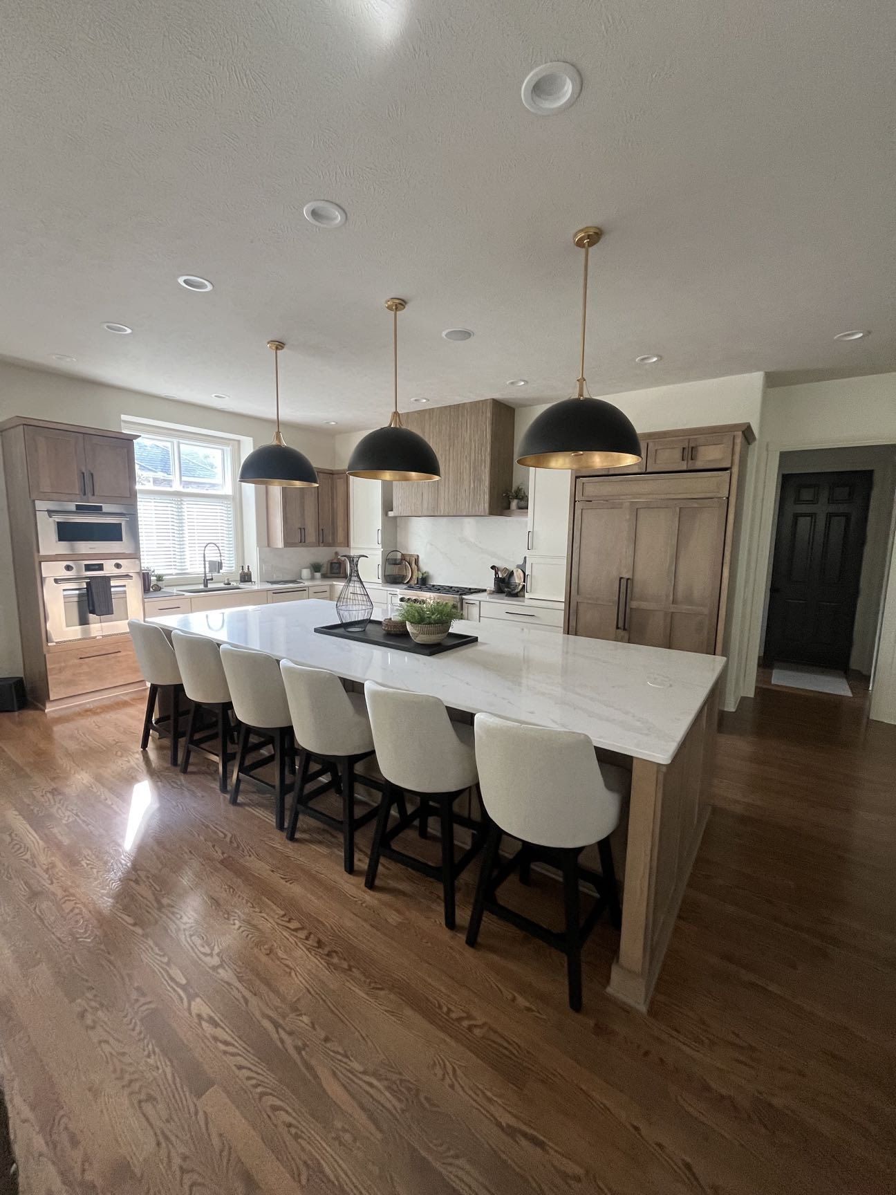 A kitchen island with white quartz counters, black pendant lighting and wood flooring in a whole-home remodel, Lincoln, NE.