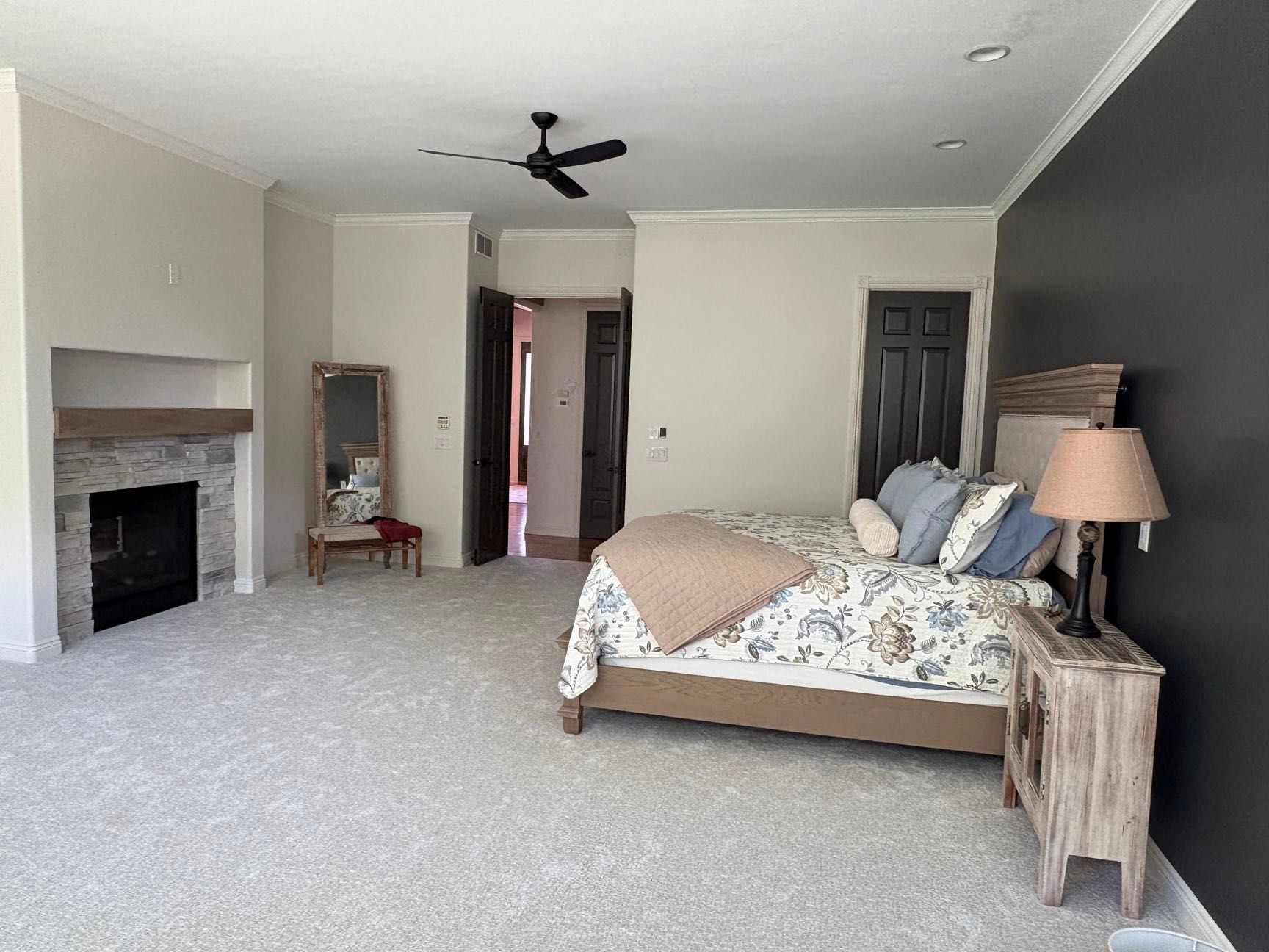 A primary bedroom with a wood bed frame, a stone fireplace, a cushioned bench and a tall leaning mirror, Lincoln, NE.