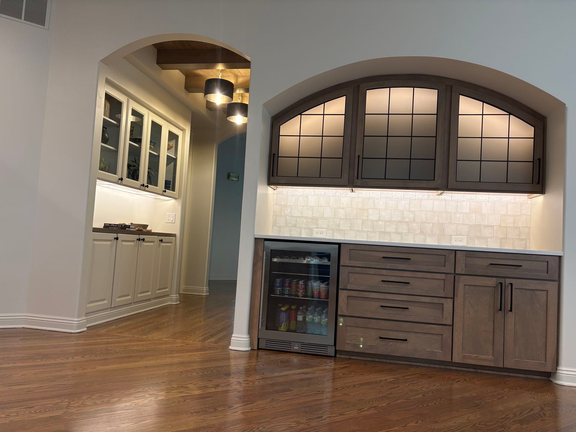 A wet bar nook with a beverage refrigerator, arched glass-front cabinetry, and a tiled backsplash, Lincoln, NE.