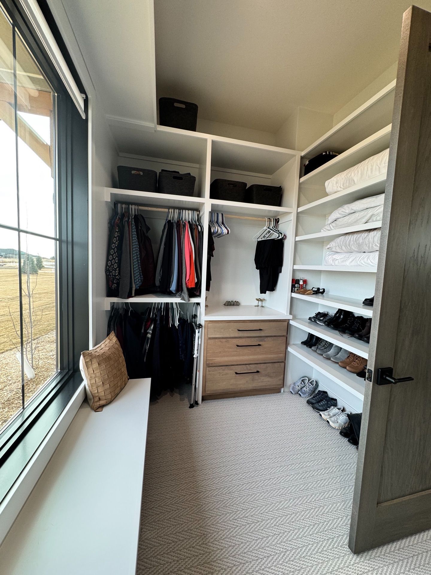 A walk in closet filled with clothes and shoes next to a window.