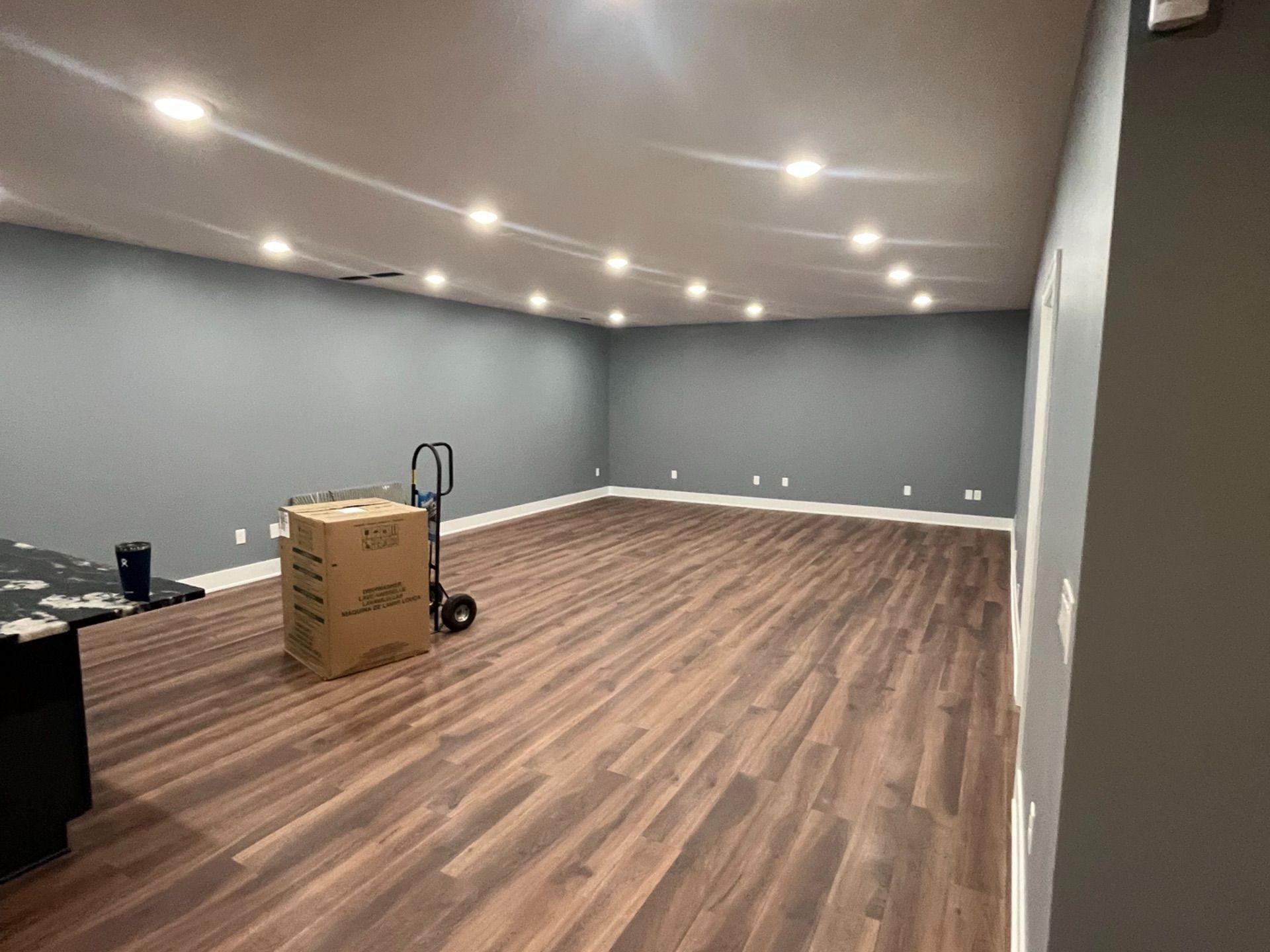 Empty room with gray walls, wooden floor, and a box on a hand truck.