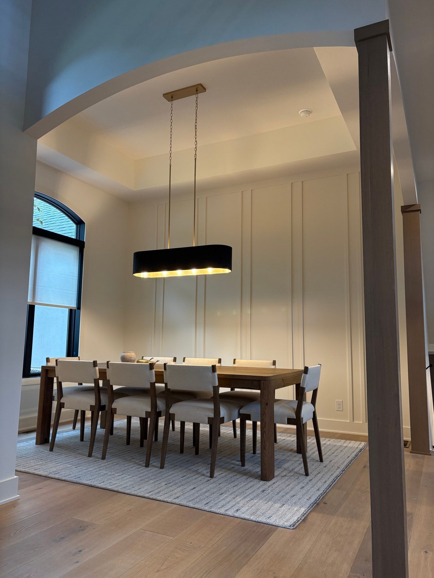 A dining room with a wood table, upholstered chairs, and a black pendant light, seen through an arched doorway, Lincoln, NE.