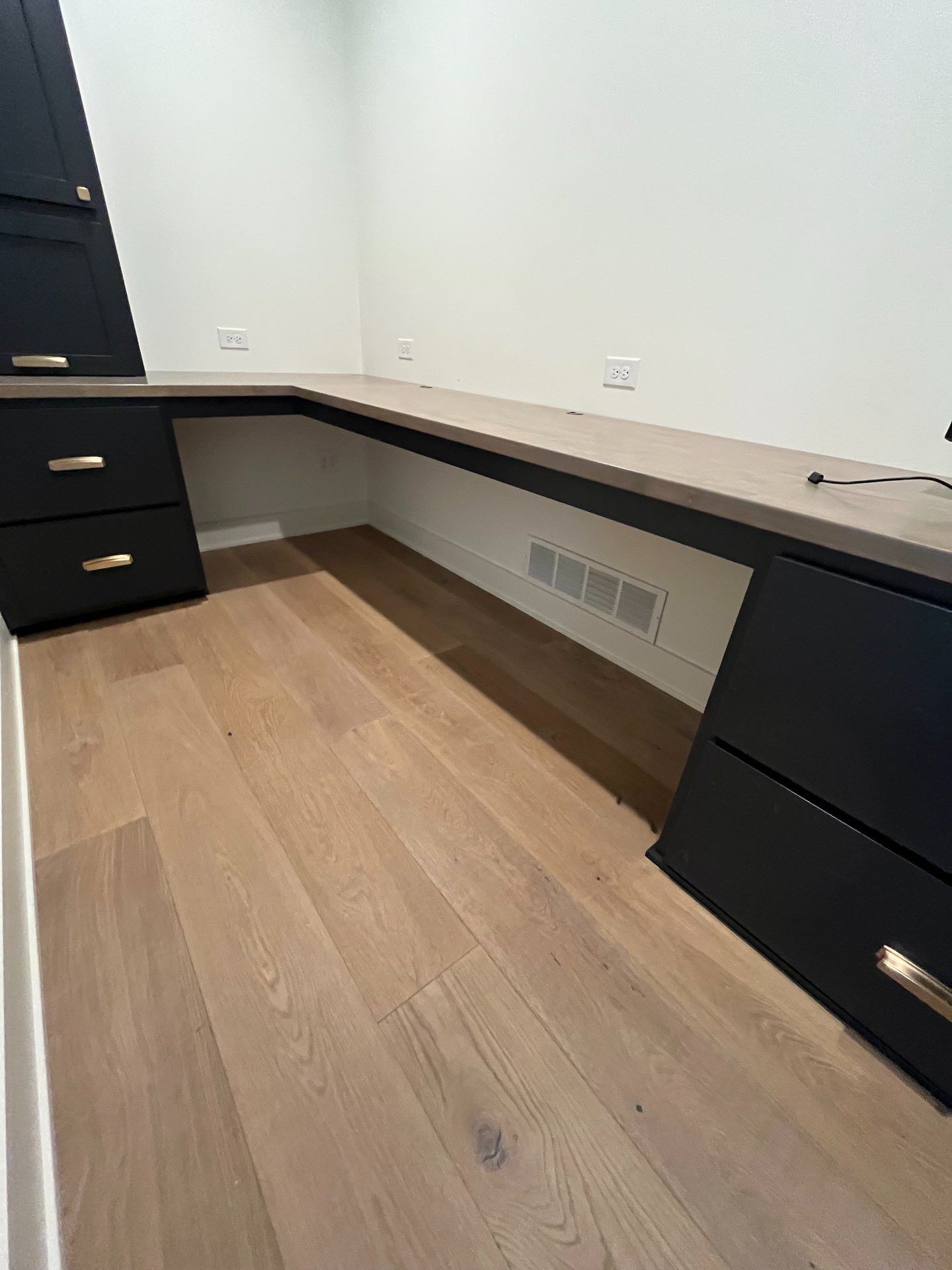 A home office nook with a built-in L-shaped desk, dark navy cabinetry with brass pulls, and wide-plank wood flooring, Lincoln, NE.