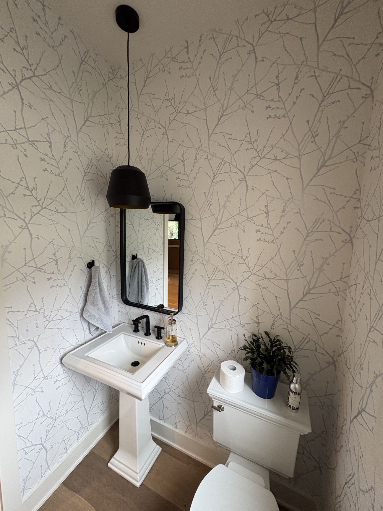A powder room with a pedestal sink, black hardware, and botanical-print wallpaper, Lincoln, NE.
