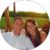 Smiling couple, outdoors, woman's arm around man's shoulder; grass, sunset in background.