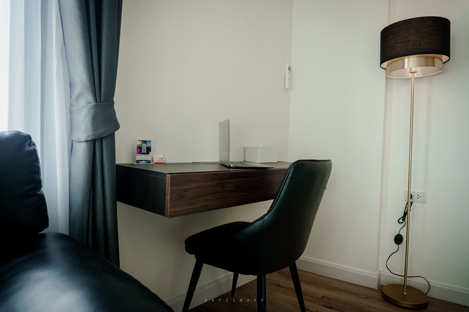 A small home office with a dark desk, chair, and a standing lamp.  A laptop sits on the desk near a window with gray curtains.