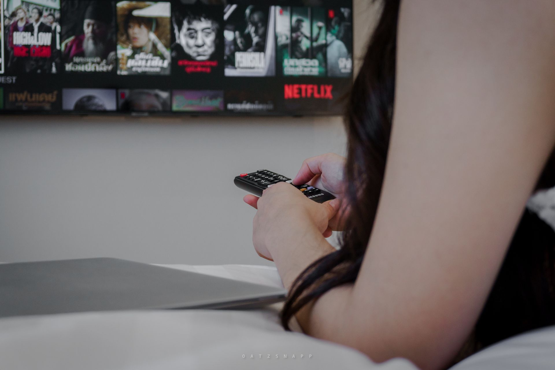 Woman using TV remote in bed, Netflix on screen.