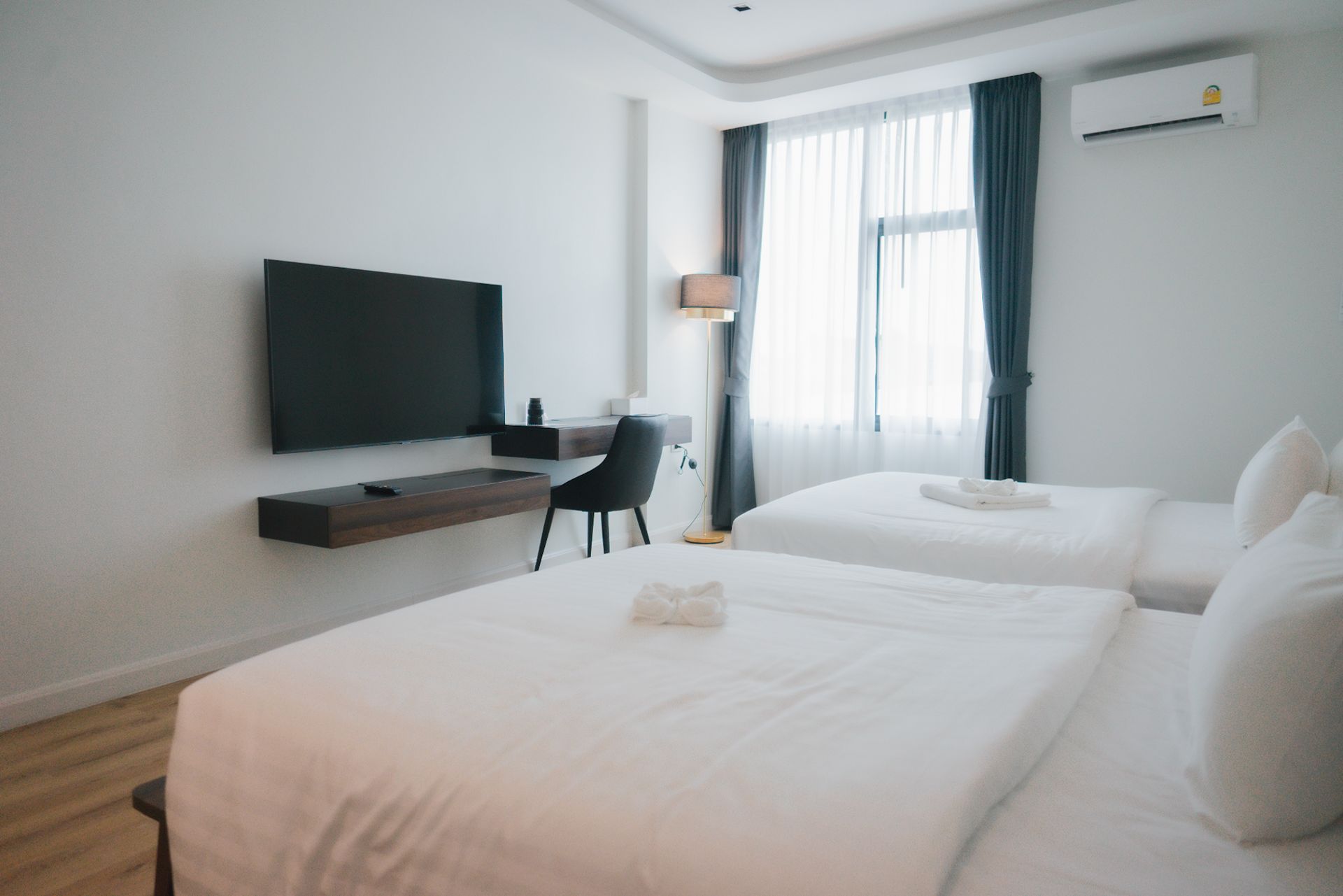 Hotel room with two beds, a desk, a mounted TV, and a window with curtains.