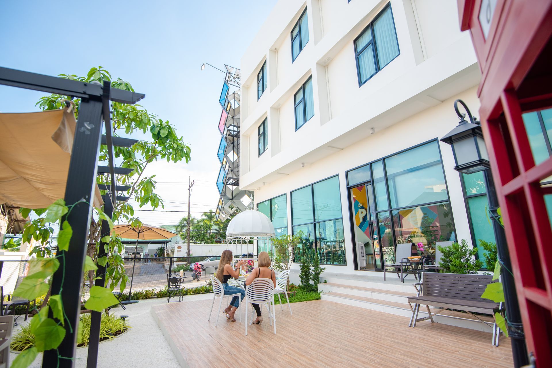 Exterior of a modern building with a seating area. Two people sit at a table. Bright, sunny day.